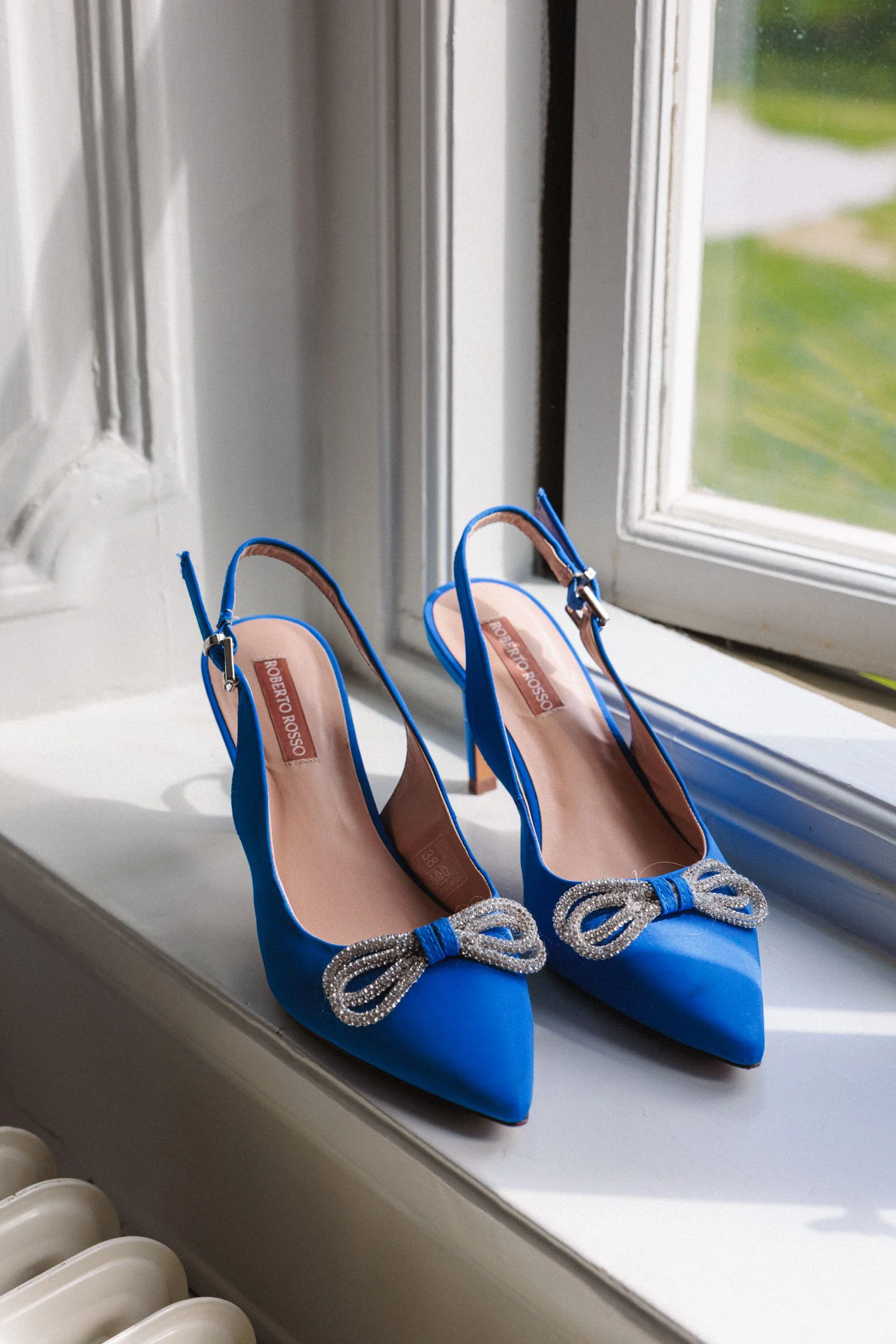Blå klackskor med rosett på, placerade på en fönsterbräda.