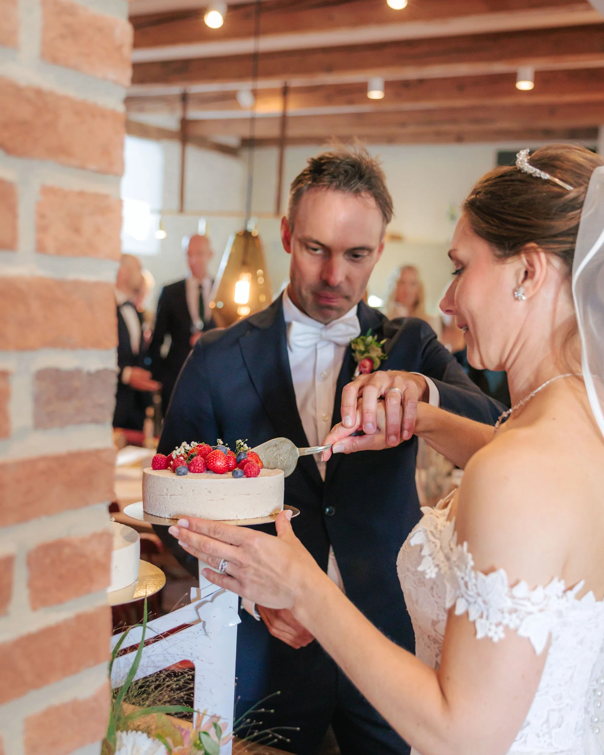 En brud och en brudgum skär tårta tillsammans på ett bröllop, omgiven av gäster.