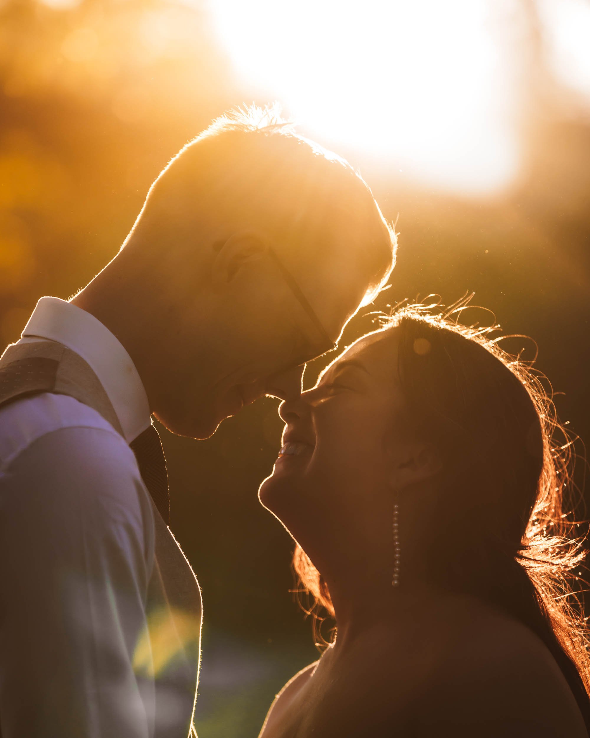 Närbild på brudpar ansikte mot ansikte i starkt golden hour-ljus med rimljus i håret