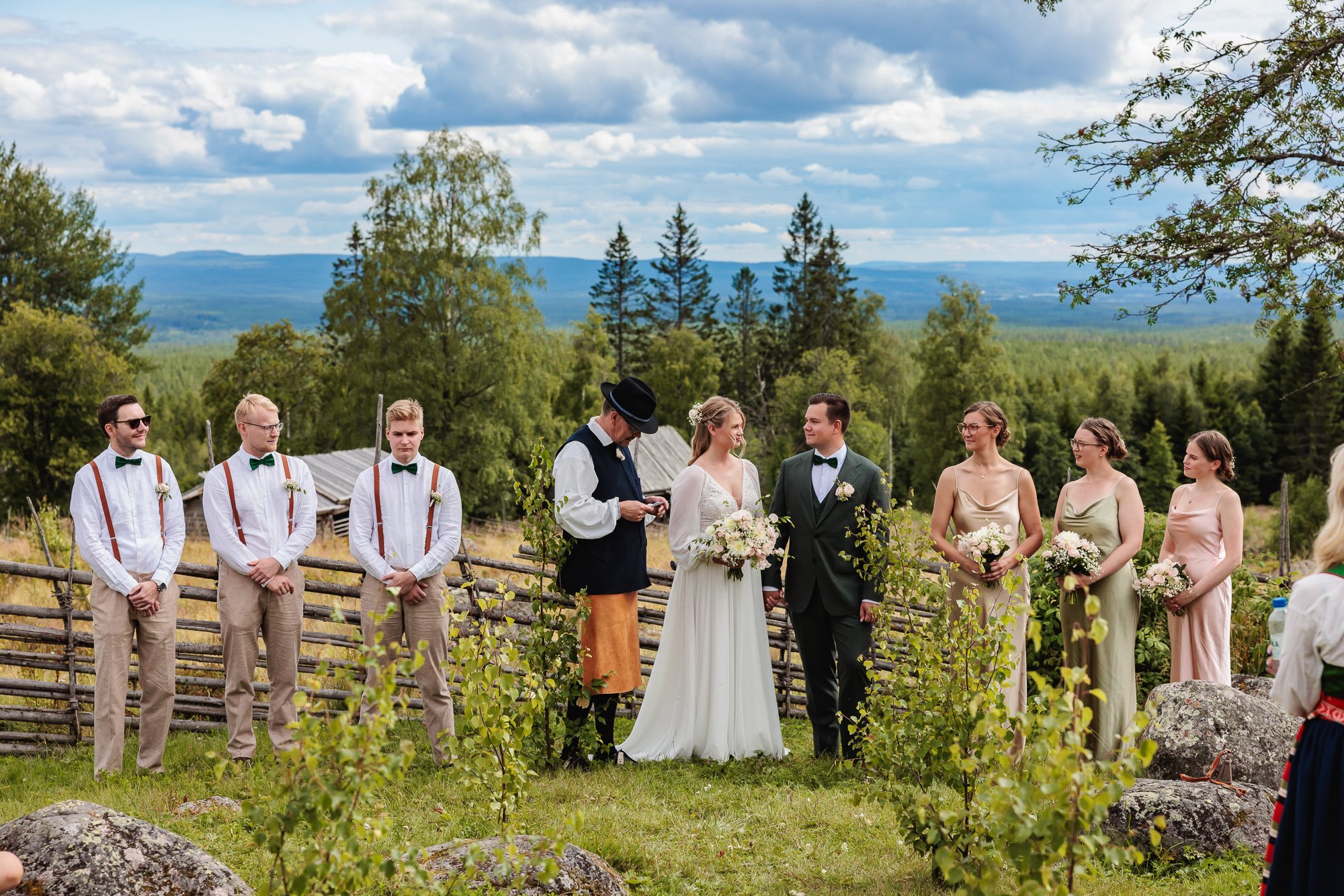 Bröllopspar under vigsel utomhus i svensk natur med brudgummar och tärnor