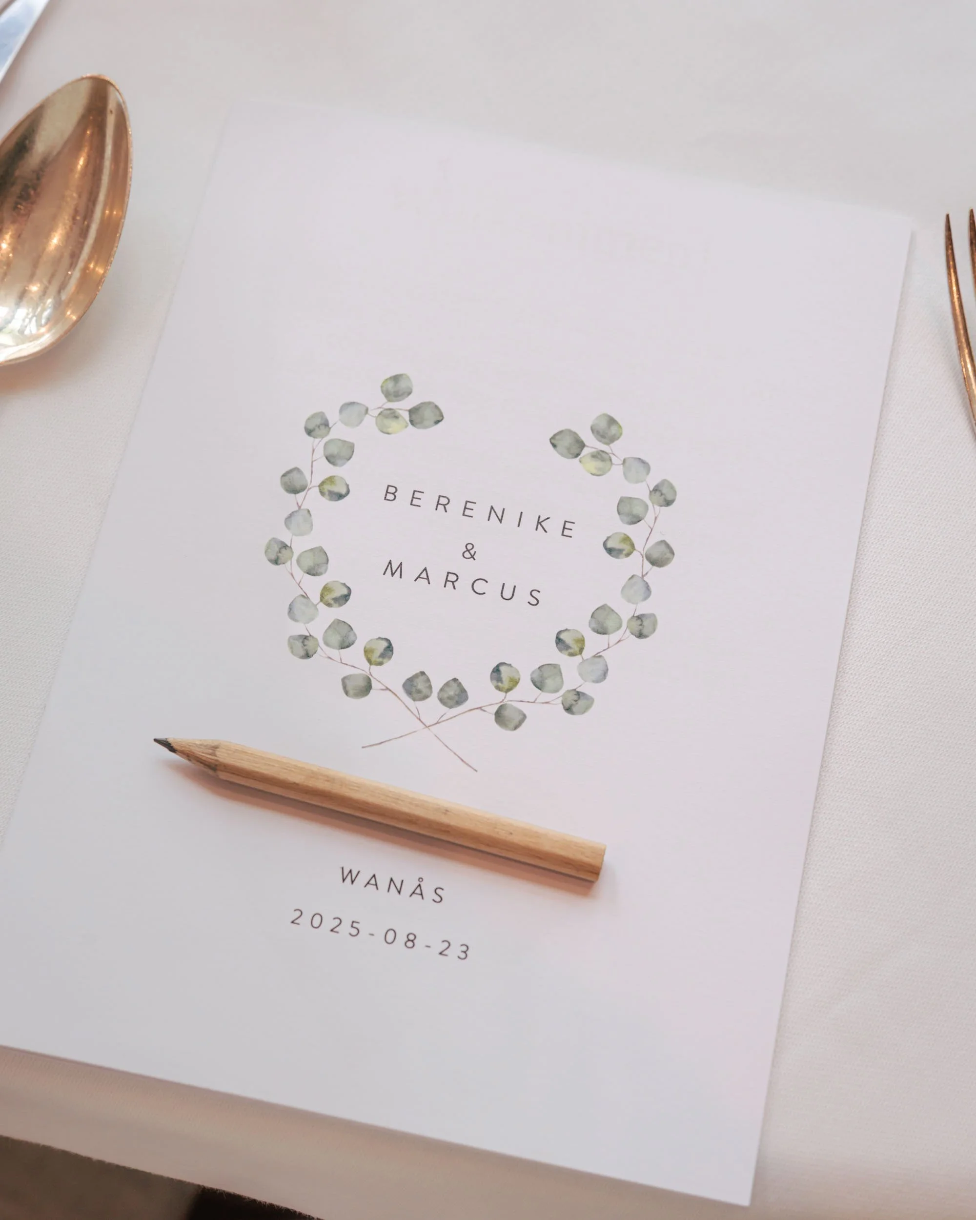 Bröllopsinbjudan med växtmotiv, namn och datum, omgiven av gaffel och sked.