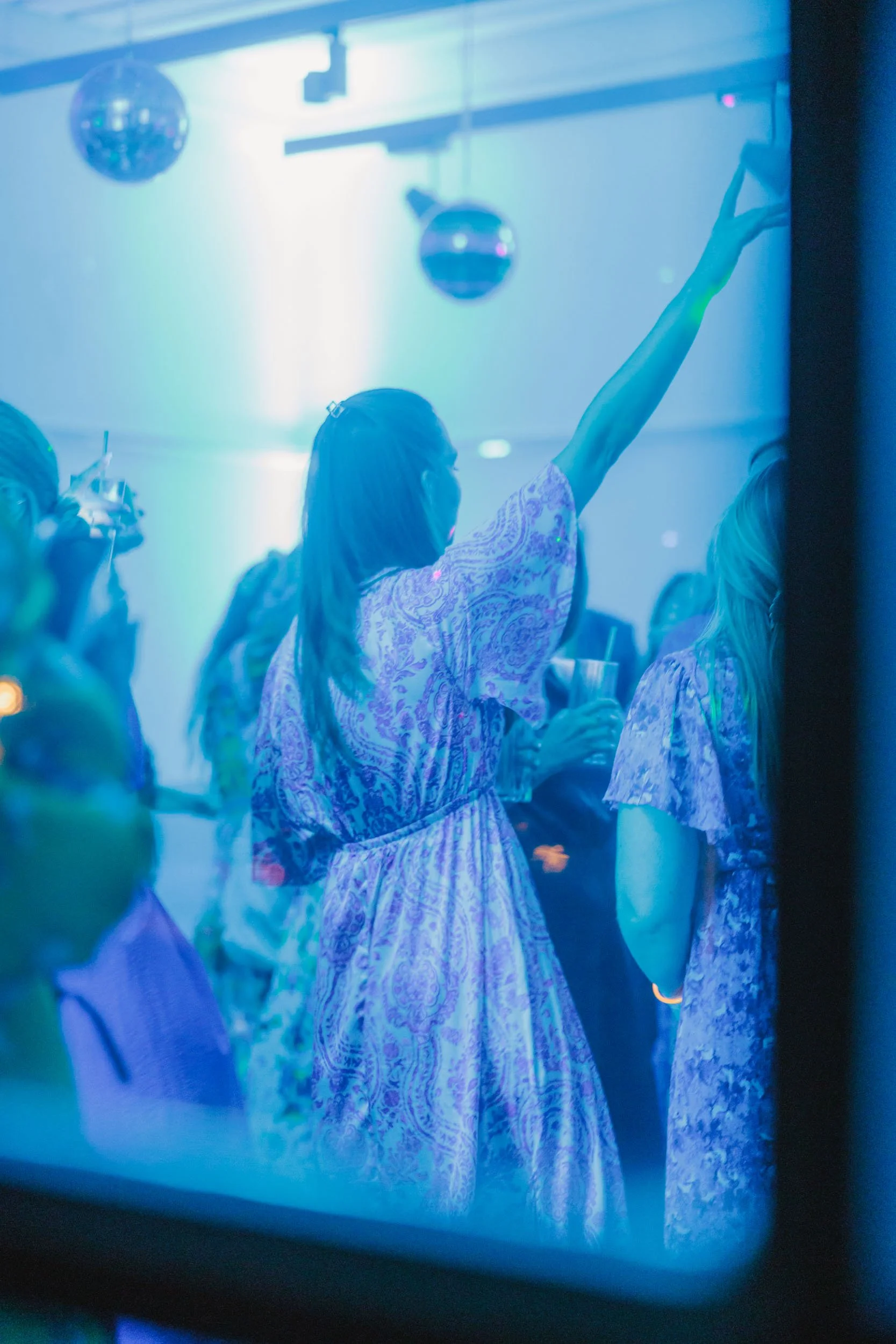 Flickor dansar och har roligt på ett dansgolv med blåa och gröna ljus, en av tjejerna håller upp handen.