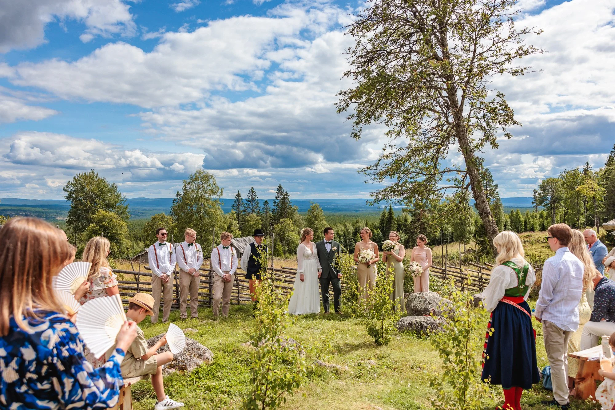 Brudpar och brudnäbb vid vigsel på fäbodvall med skog och dalar i bakgrunden