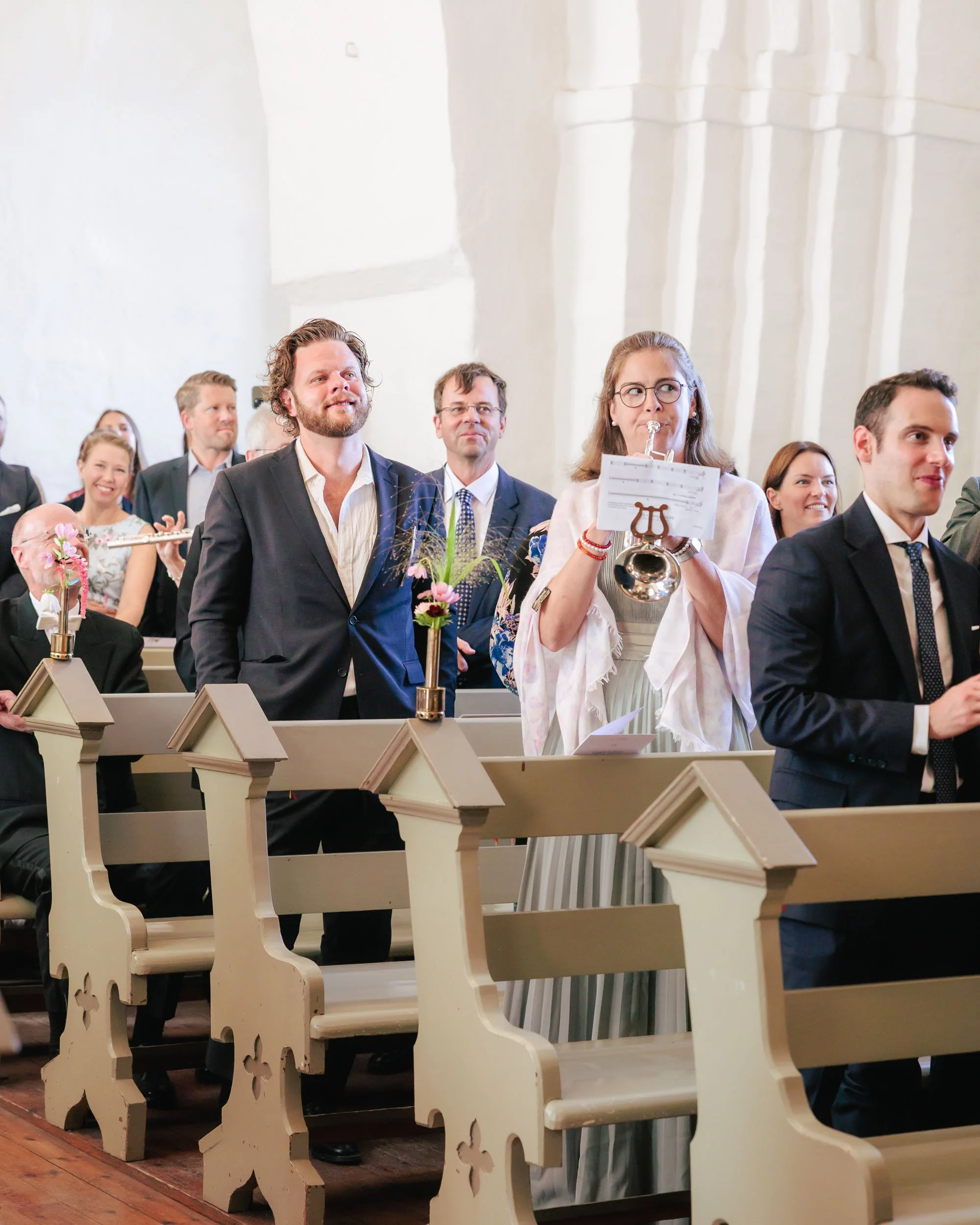 Människor i kyrka som spelar och lyssnar på ett musikstycke under en ceremoni.