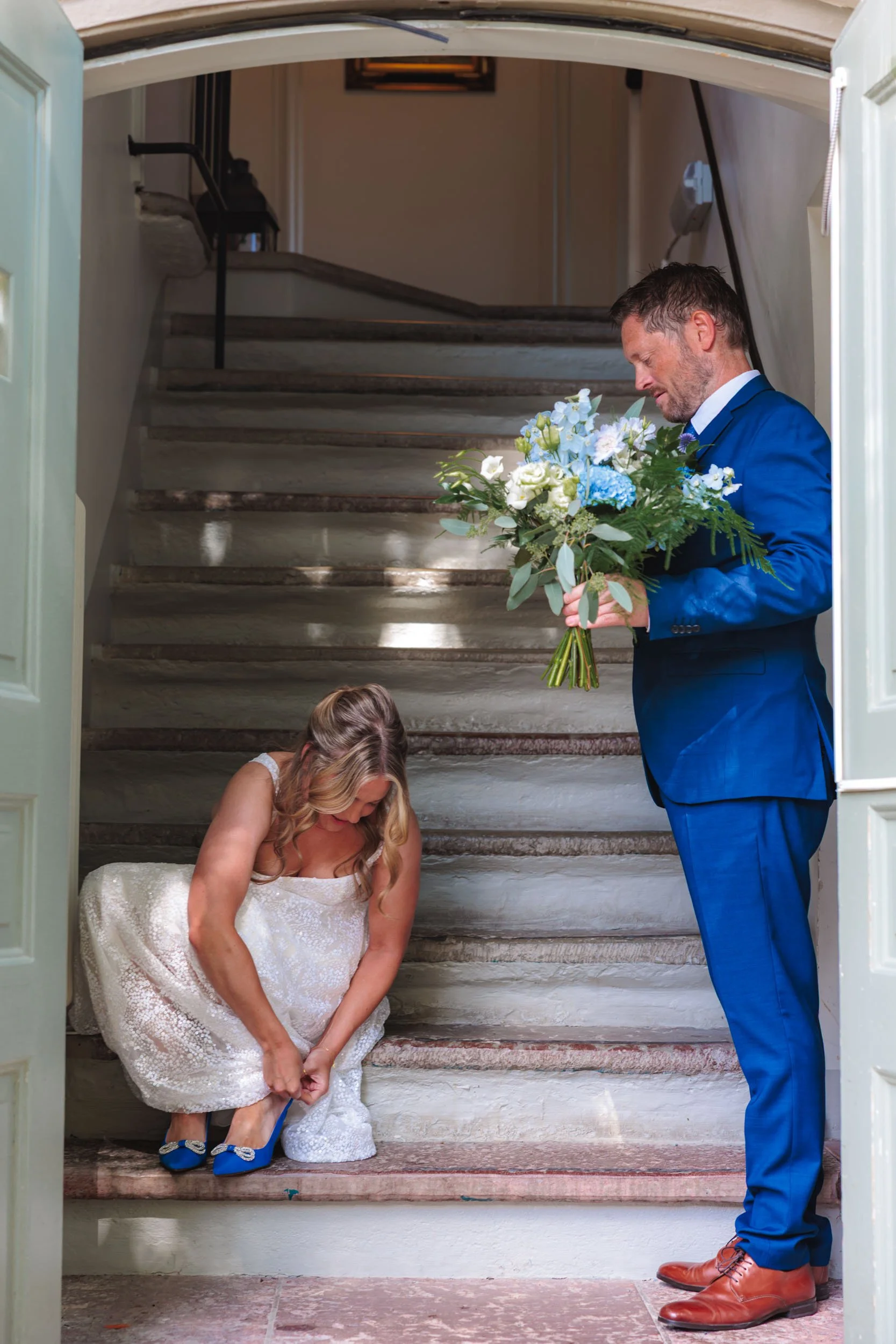 En man i blå kostym ger en blomsterbukett till en kvinna i bröllopsklänning på en trappa.