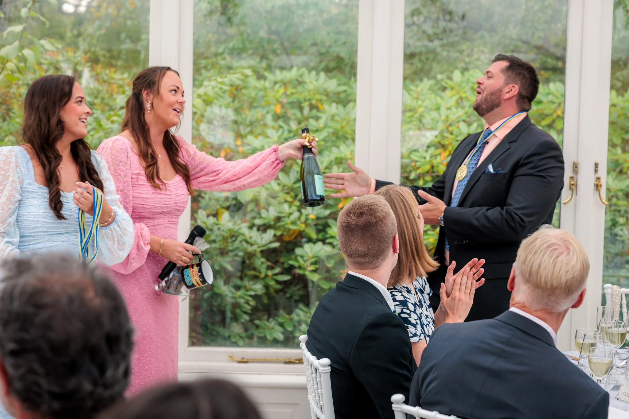 Gäster överlämnar champagneflaska som inslag under bröllopsmiddag med applåderande publik
