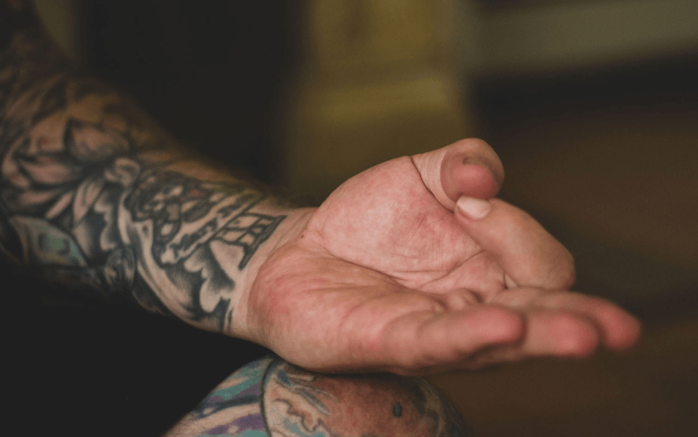 A tattooed man's hand in a mudra