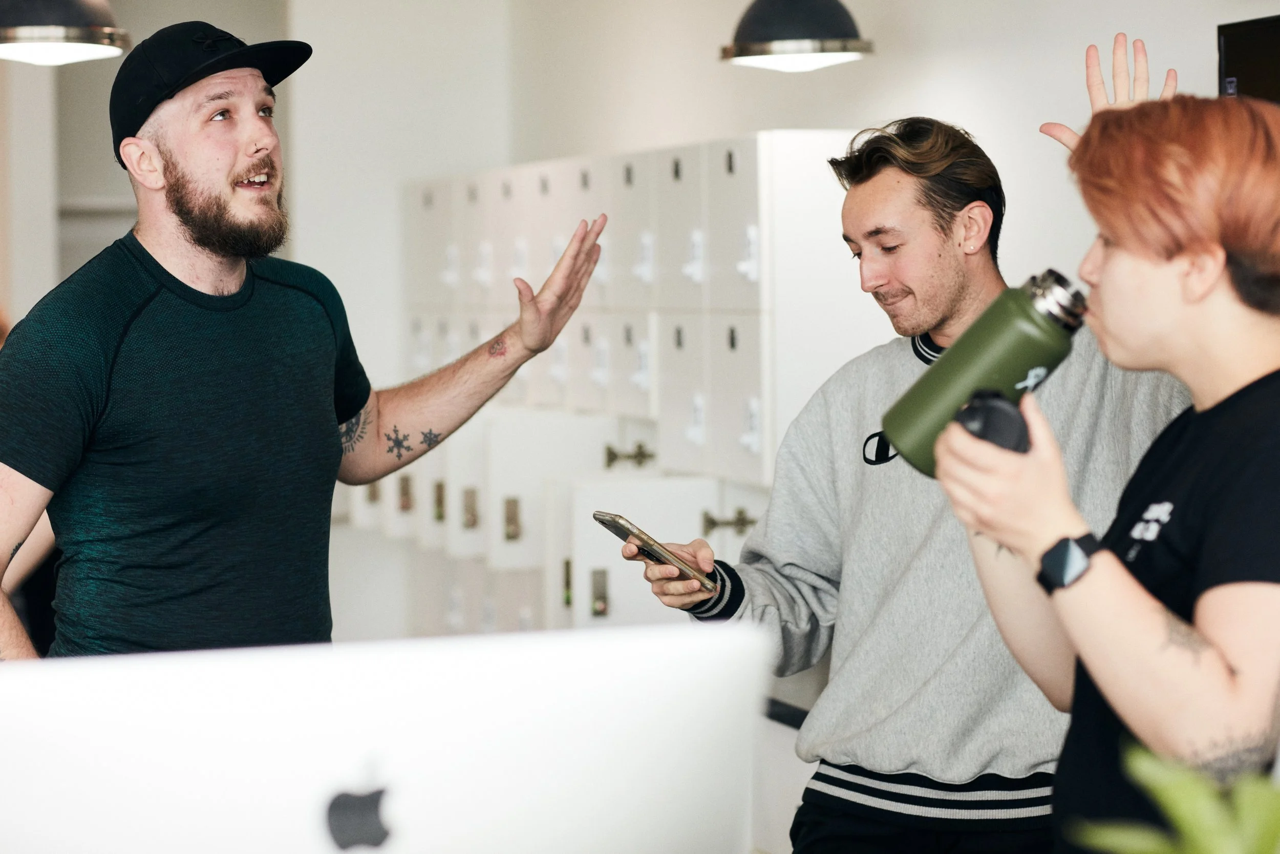 Three people standing in a studio, one holding a phone and another drinking from a water bottle