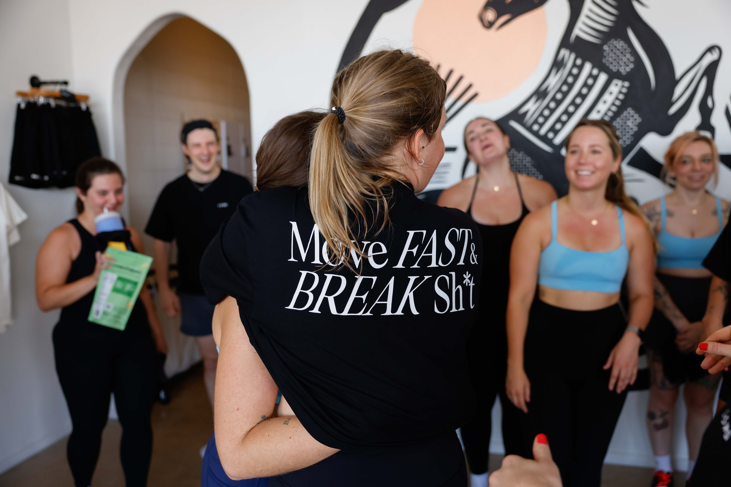 Group of people at a fitness studio and two women hugging.