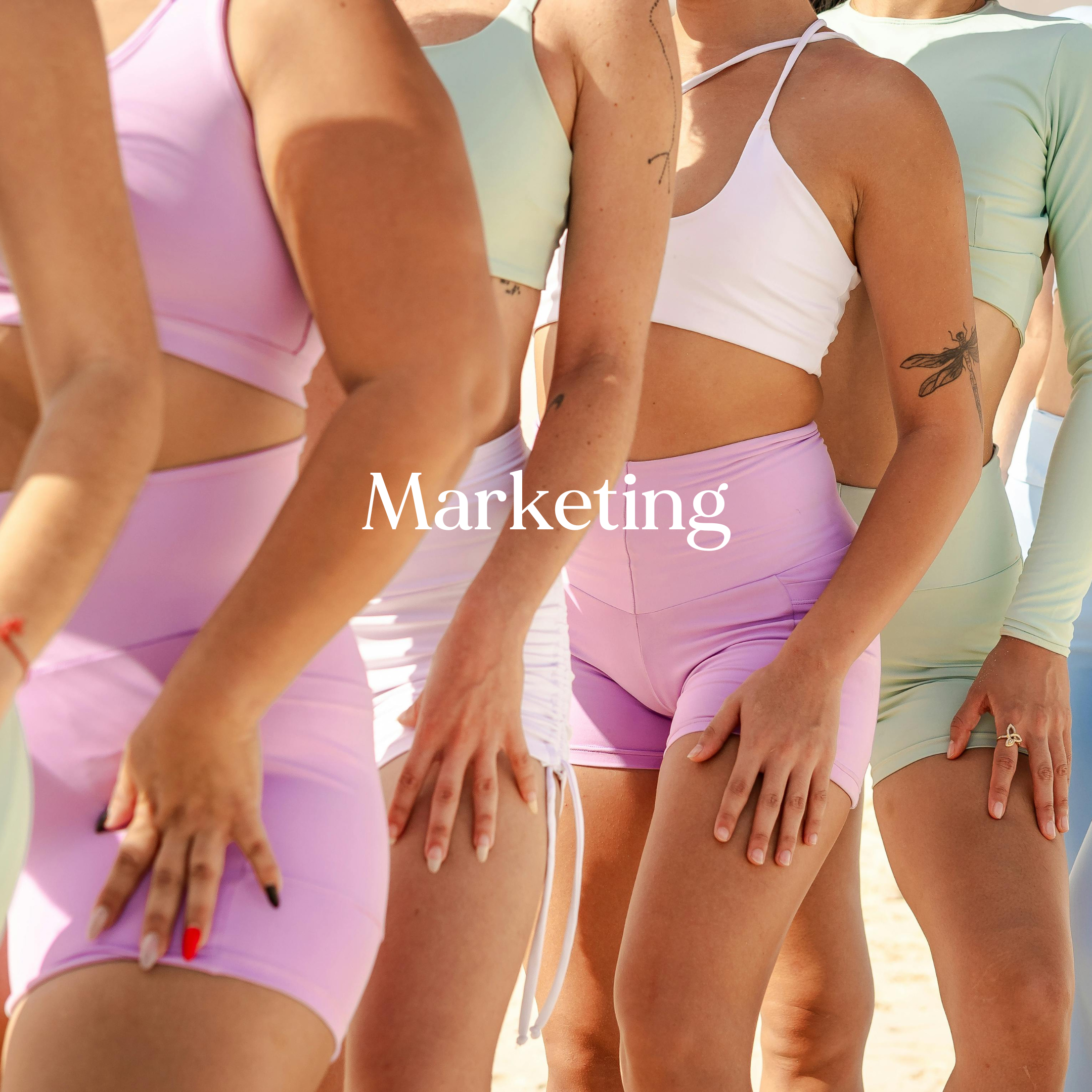 Close-up of a group of women standing in a line, wearing pastel-colored athletic clothes and showing various tattoos and toned bodies