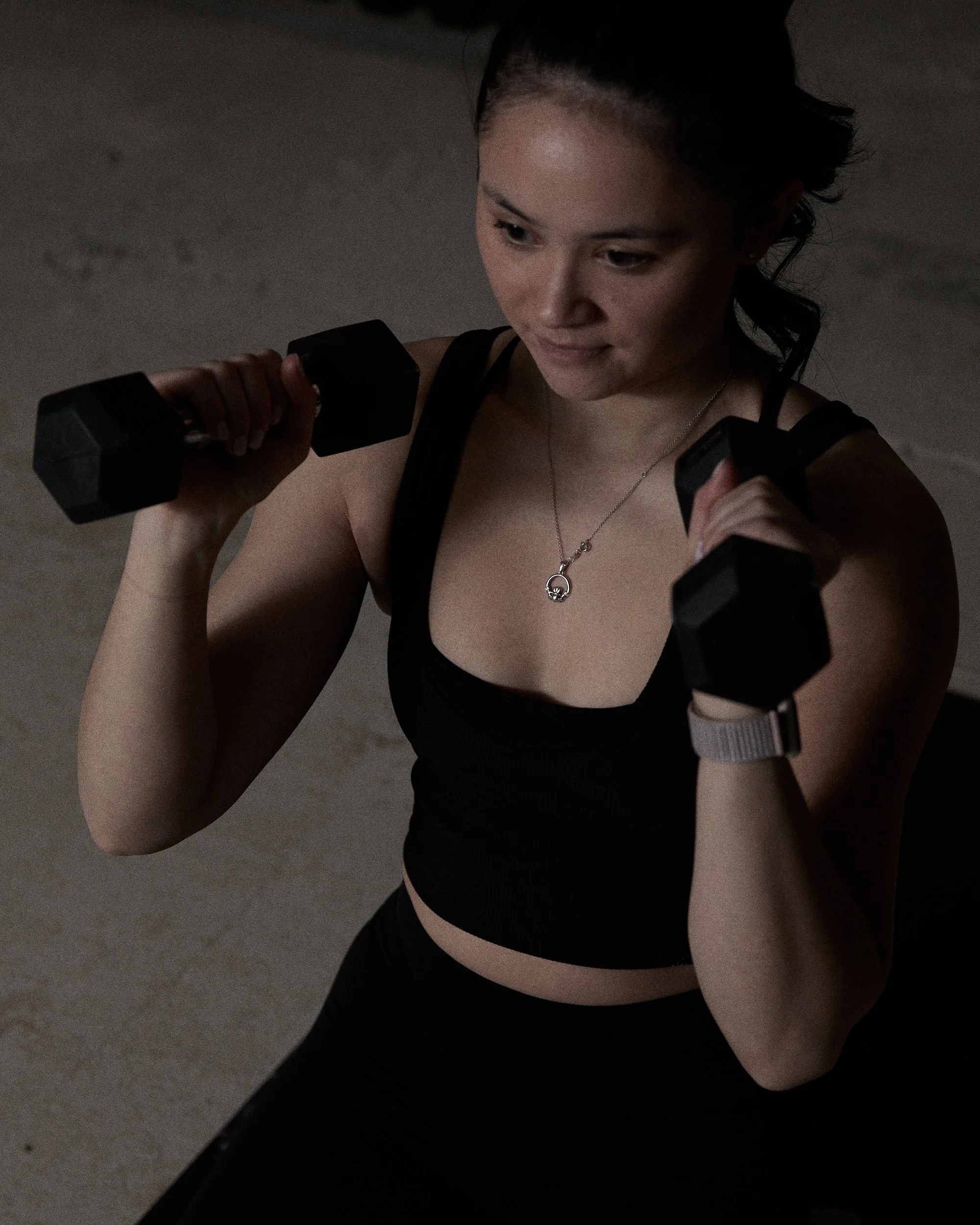 A young woman holding dumbbells at Sodium Fit, preparing for her workout.