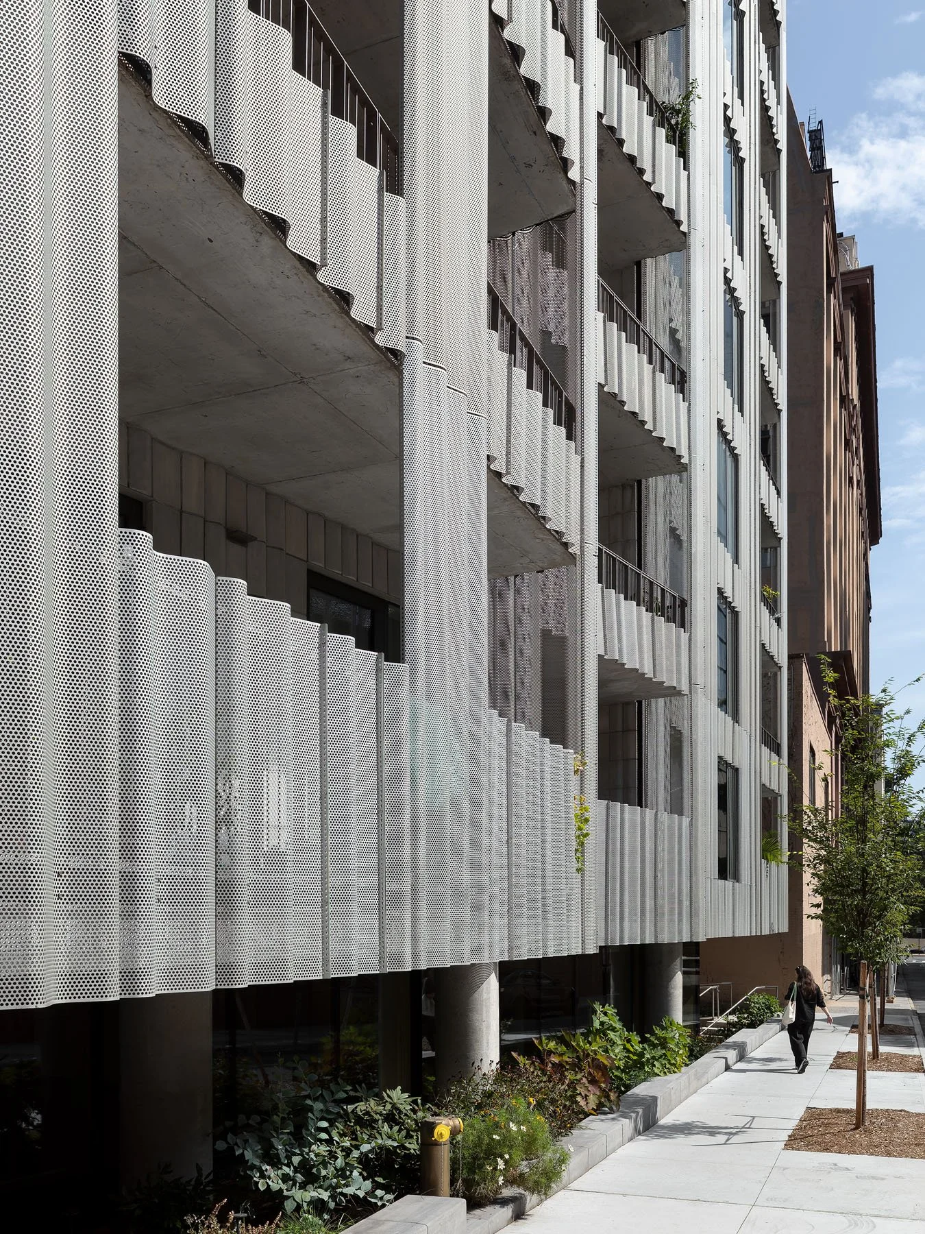 9 Chapel perforated aluminum facade along sidewalk with scalloped balcony soffits and a pedestrian figure, by SO–IL - architectural photographer New York