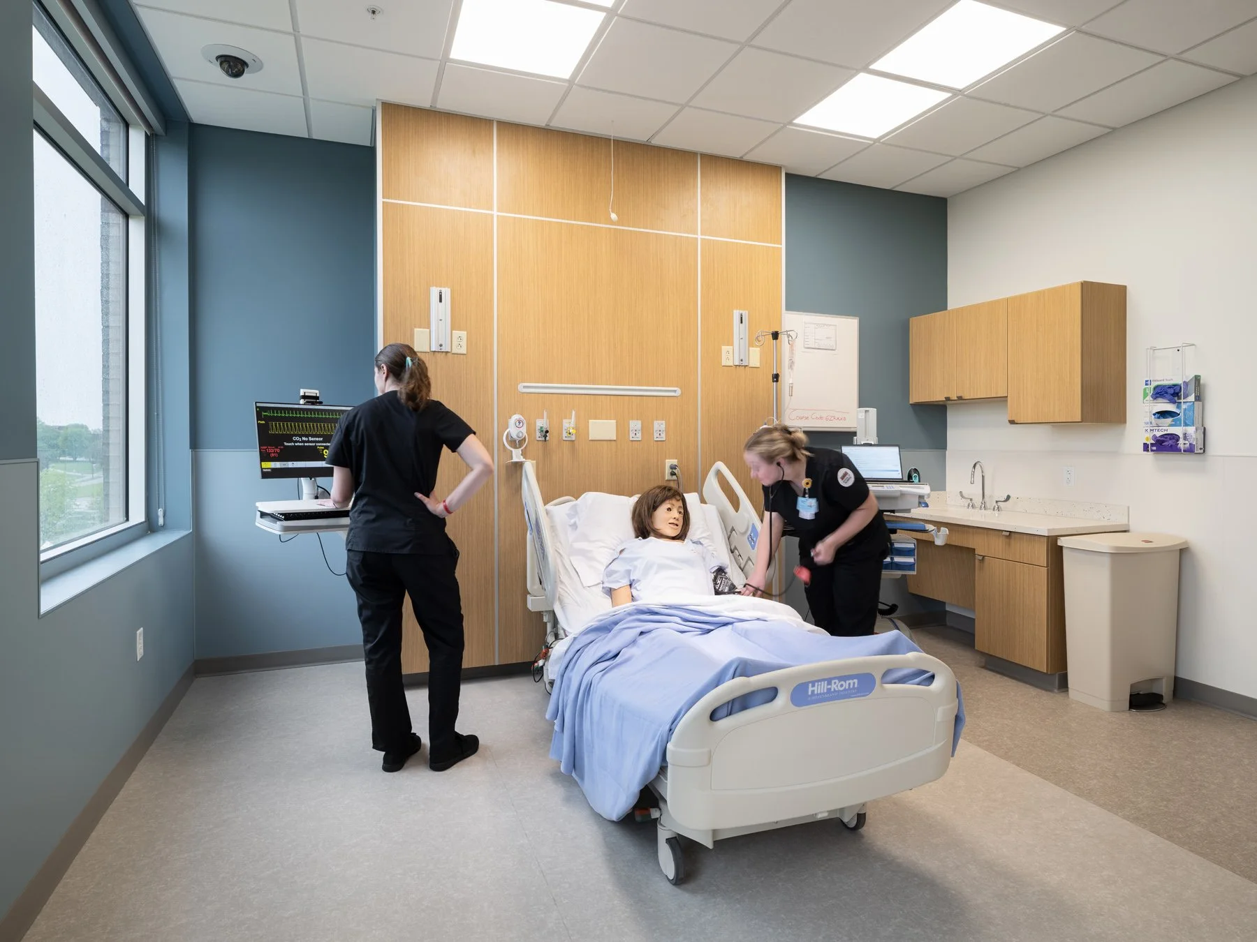 SIUE Health Sciences nursing simulation patient room with a manikin and students by Christner, Edwardsville Illinois - architectural photographer St. Louis