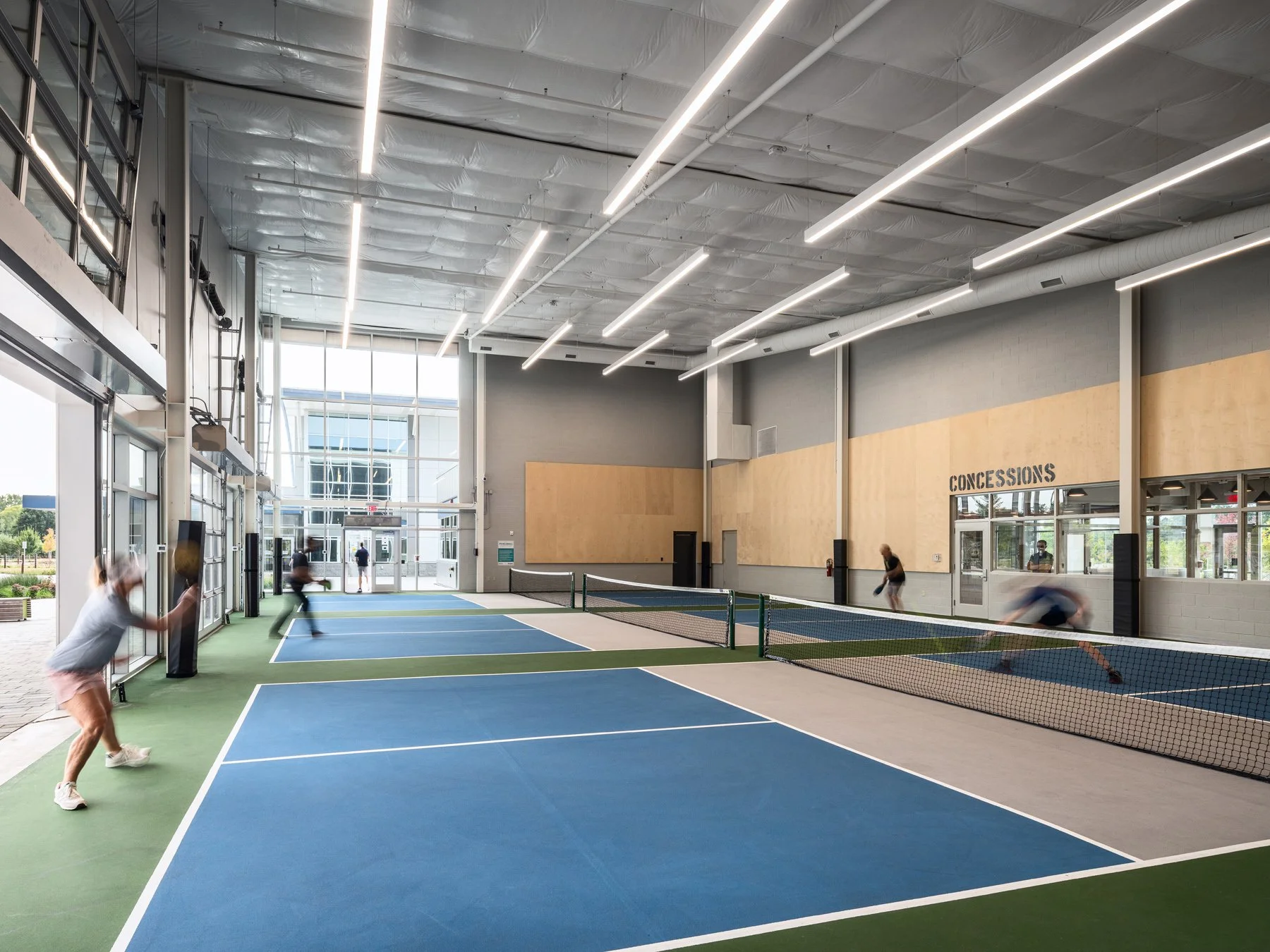 Kinetic Park interior pickleball courts with players and concessions signage, by JEMA - architectural photographer St. Louis Missouri
