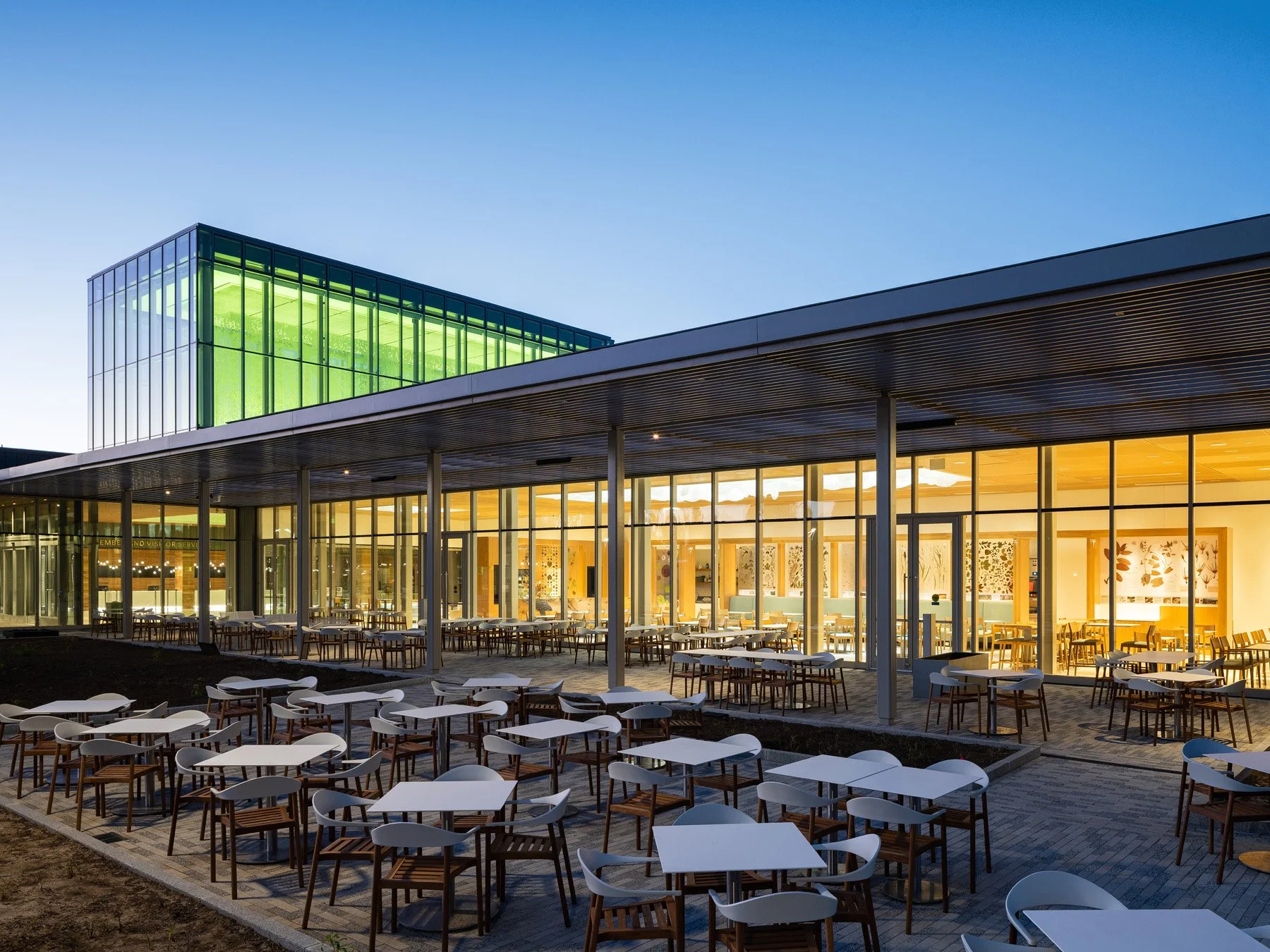 Sassafras Cafe at twilight with patio tables and a glowing green glass cube by Ayers Saint Gross - architectural photographer St. Louis Missouri