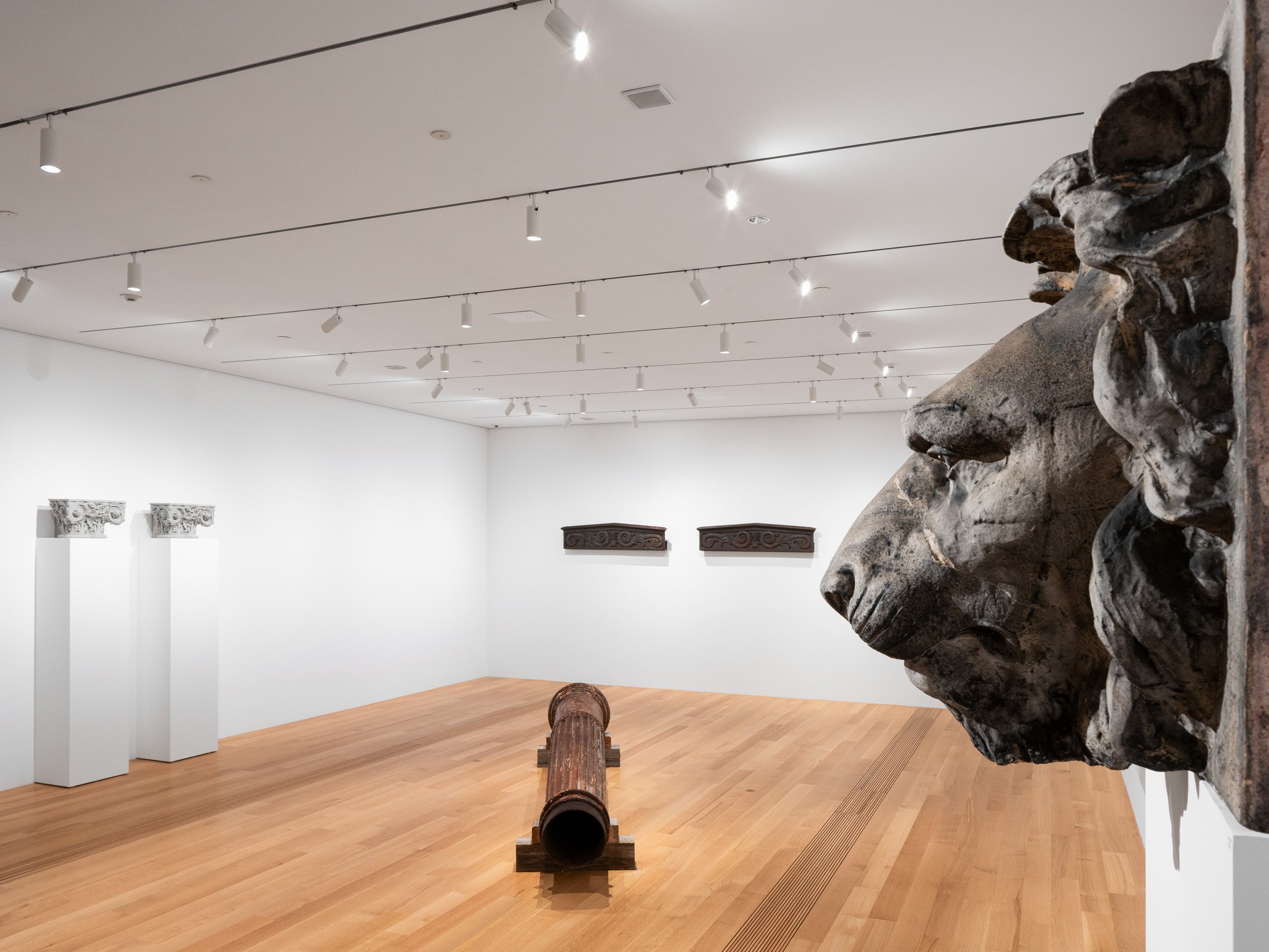Pulitzer Arts Foundation interior gallery showing a large salvaged lion-head ornament in the foreground with carved capitals on pedestals across the room, by Tadao Ando, St. Louis Missouri - architectural photographer St. Louis Missouri