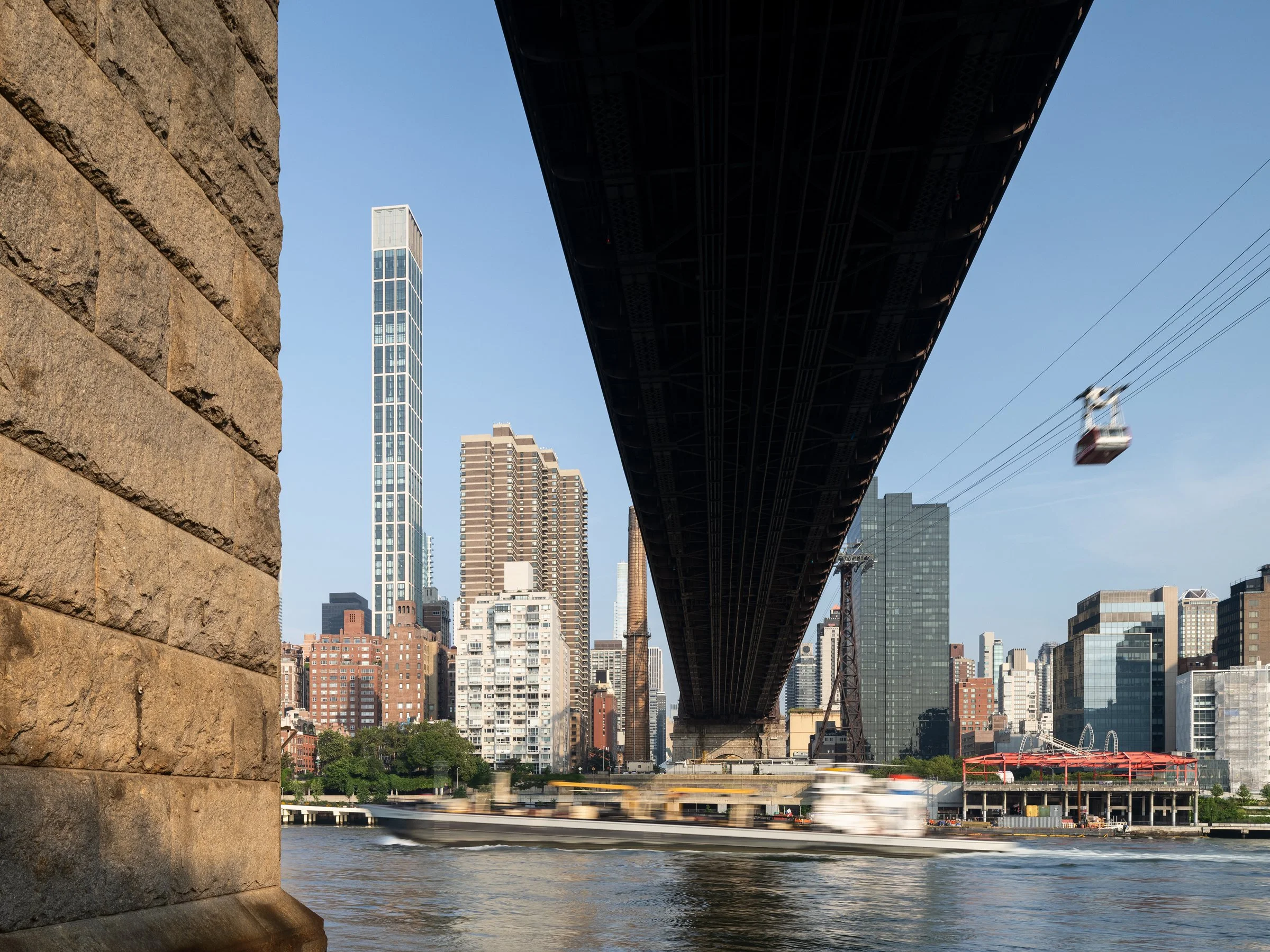 Sutton Tower viewed from beneath the Queensboro Bridge with a ferry passing on the East River and the Roosevelt Island Tram above, by Thomas Juul-Hansen, New York New York - architectural photographer