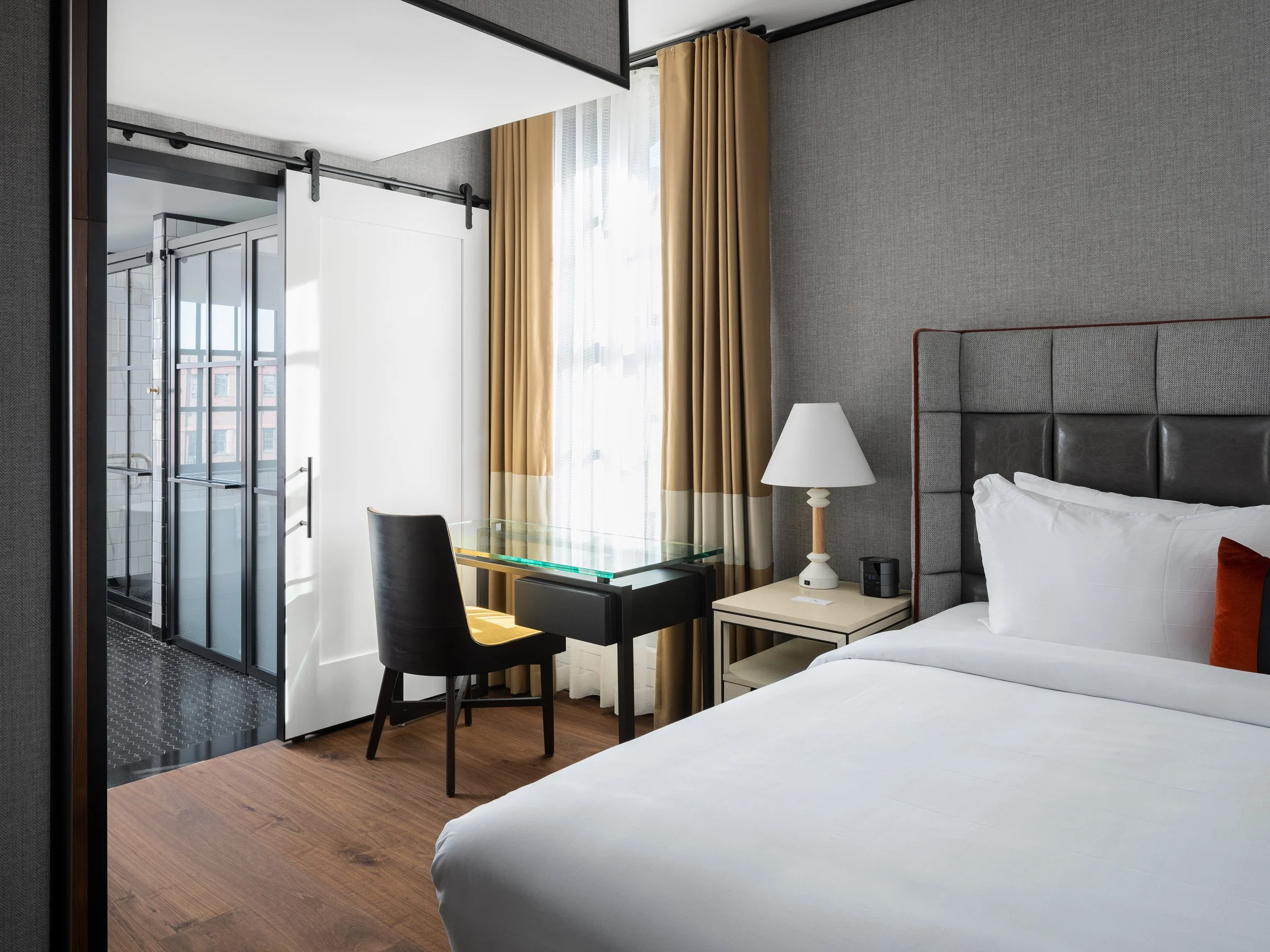 21c Museum Hotel interior guest room with a king bed and glass writing desk, a sliding barn door opening to a glass enclosed bathroom, by Perfido Weiskopf Wagstaff + Goettel and Bill Rooney Studio - architectural photographer St. Louis Missouri