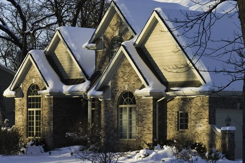 Brick McMansion with triple pointed gabled dormers and arched windows covered in snow under low winter sun, Chicago Illinois exurbs
