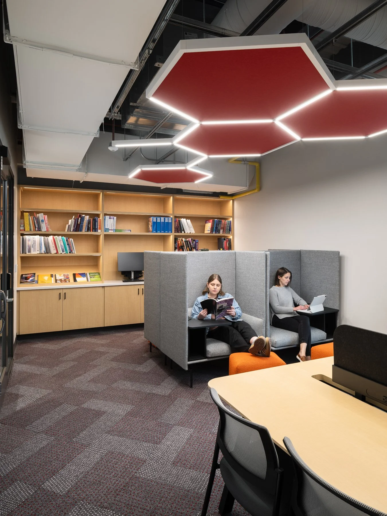 Regional Workforce Innovation Center library study nook with gray upholstered pods, wood shelving, and hexagonal red acoustic ceiling panels, Wentzville, Missouri, by JEMA - architectural photographer St. Louis Missouri