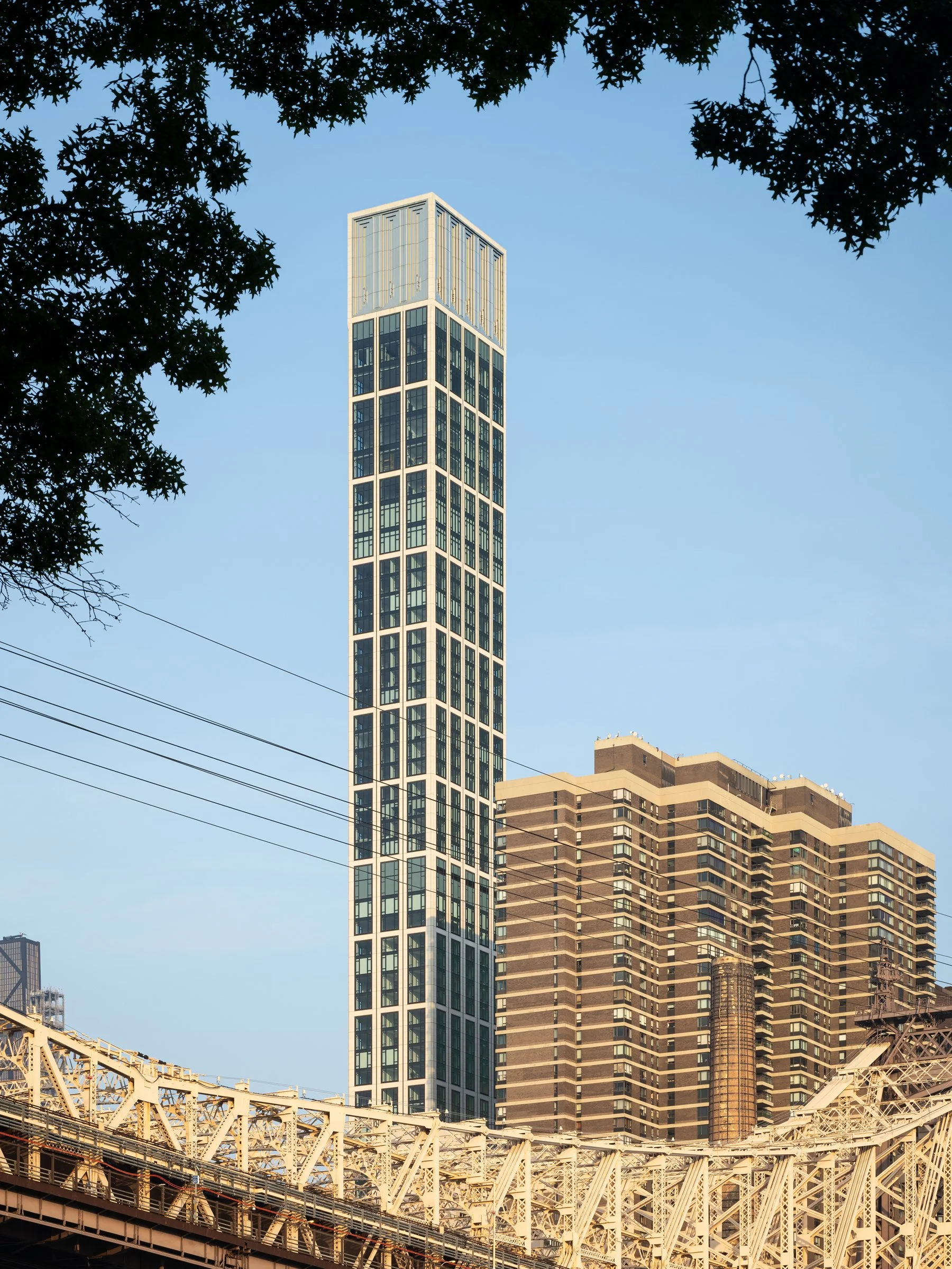 Sutton Tower at golden hour framed by trees and the steel of the Queensboro Bridge, the slender limestone skyscraper catching warm light, by Thomas Juul-Hansen, New York New York - architectural photographer