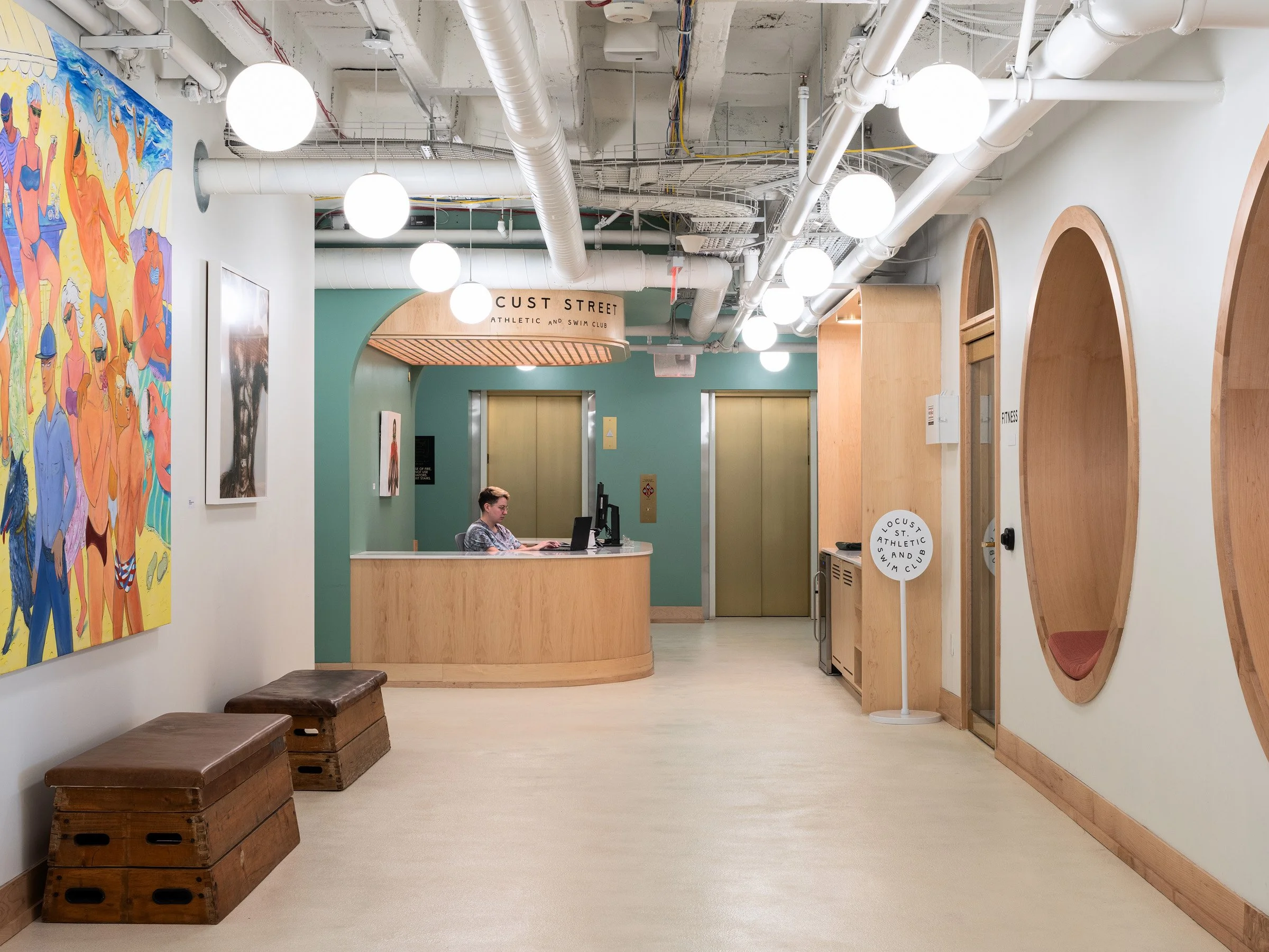 Locust Street Athletic and Swim Club interior reception desk with curved signage, an exposed pipe ceiling and a figurative mural, at the 21c Museum Hotel by Perfido Weiskopf Wagstaff + Goettel and Hufft - architectural photographer St. Louis Missouri