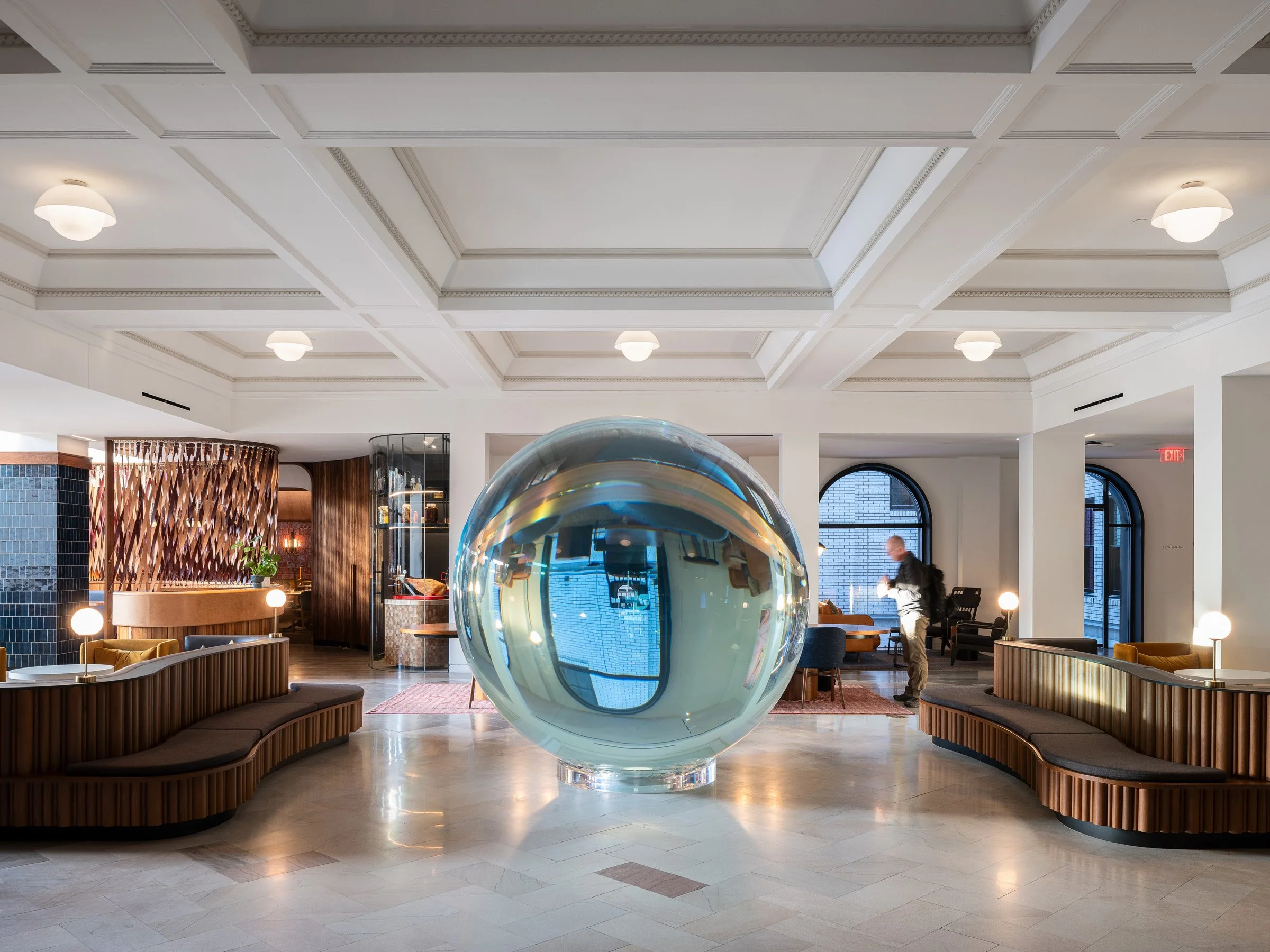 21c Museum Hotel interior lobby with a large reflective glass sphere sculpture beneath a white coffered plaster ceiling and curved wood banquettes, by Perfido Weiskopf Wagstaff + Goettel and Hufft - architectural photographer St. Louis Missouri