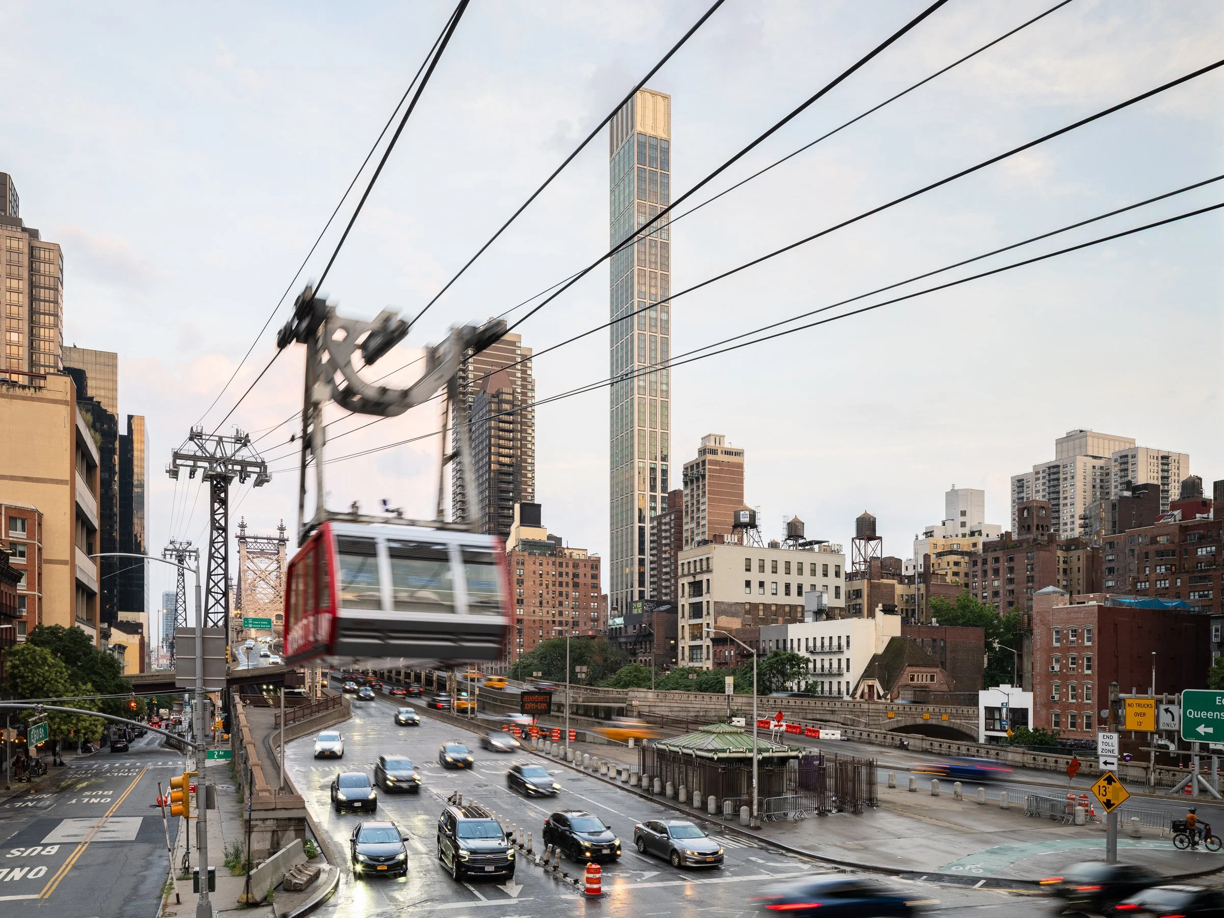 Sutton Tower seen from the street at dusk with the red Roosevelt Island Tram crossing overhead above traffic on the approach to the Queensboro Bridge, by Thomas Juul-Hansen, New York New York - architectural photographer