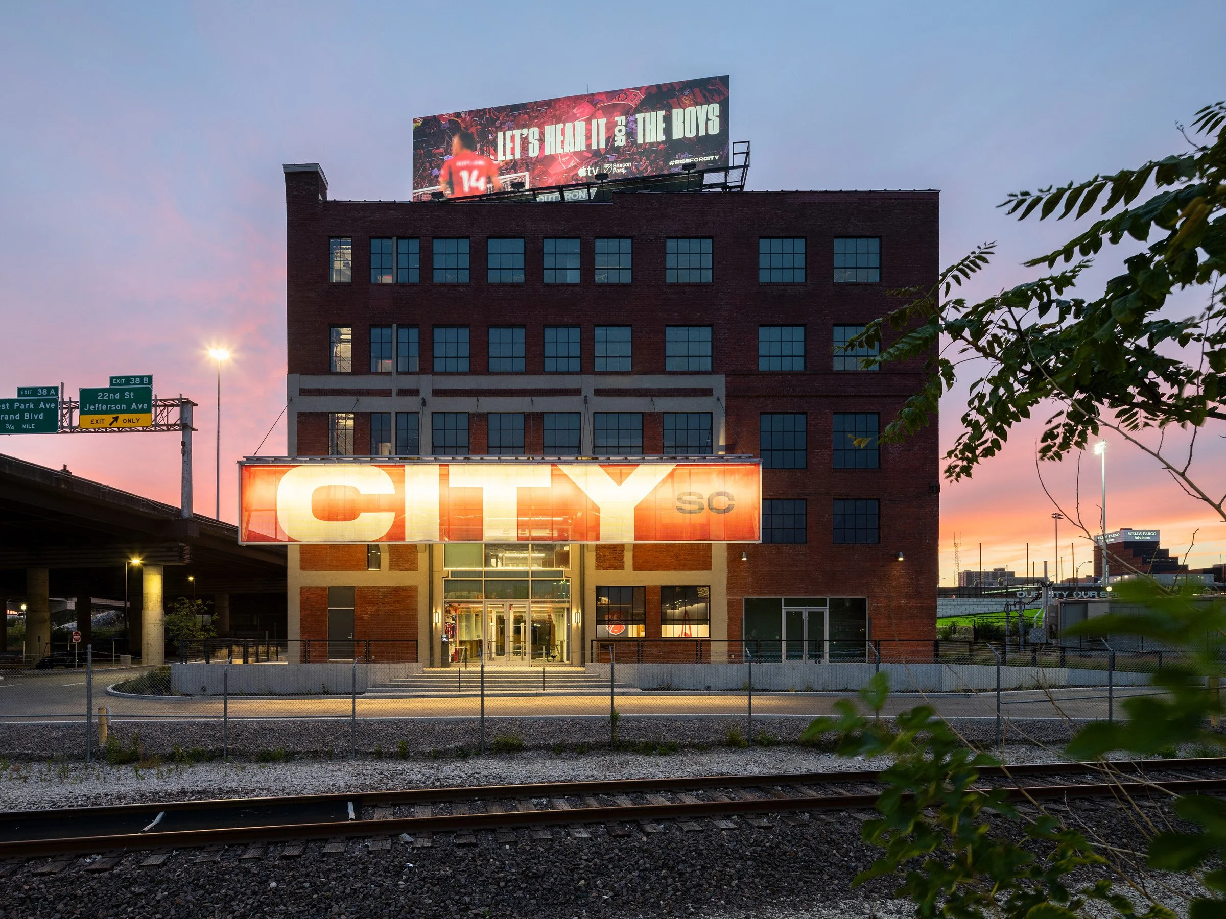 Energizer Park renovated brick building exterior at dusk with an illuminated CITY SC marquee and rail lines in the foreground, by Christner Architects, St. Louis Missouri - architectural photographer St. Louis Missouri