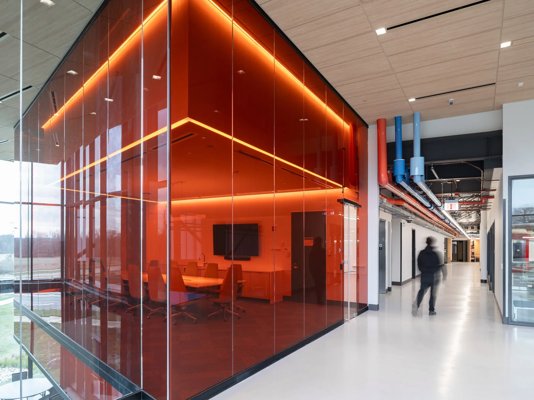 Regional Workforce Innovation Center second-floor corridor with a red glass conference room volume and exposed color-coded mechanical piping overhead, Wentzville, Missouri, by JEMA - architectural photographer St. Louis Missouri