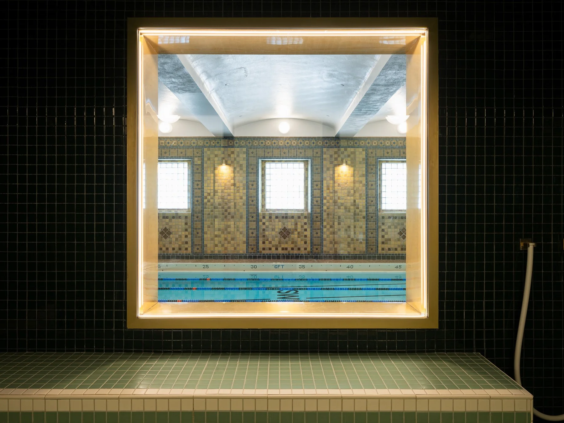 Locust Street Athletic and Swim Club interior view through a gold framed window into the historic lap pool, at the 21c Museum Hotel by Perfido Weiskopf Wagstaff + Goettel with tile by Rookwood Pottery - architectural photographer St. Louis Missouri