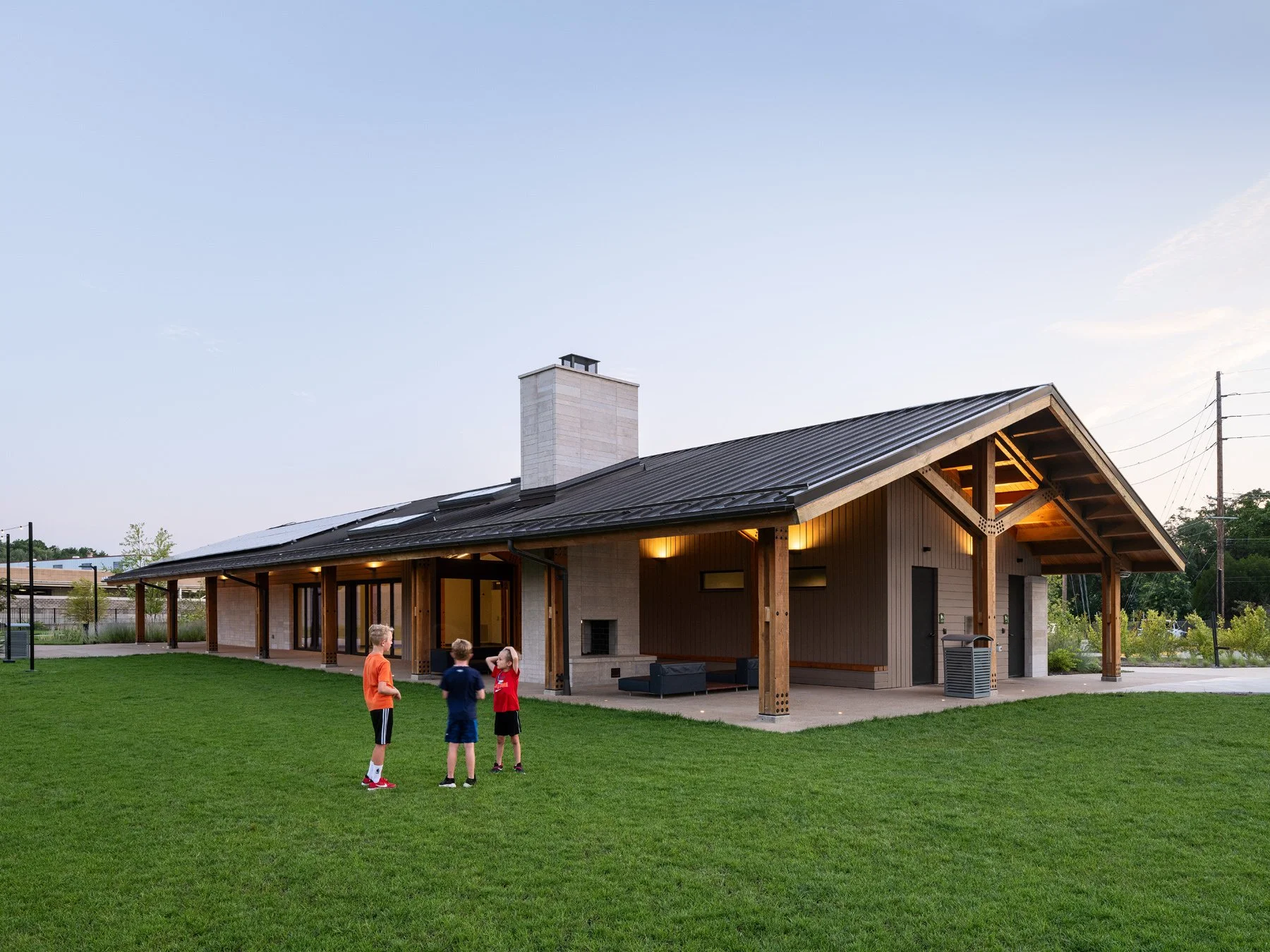 Brentwood Park Event Pavilion lawn facade at dusk with masonry chimney and lit terrace, by Christner - architectural photographer St. Louis Missouri