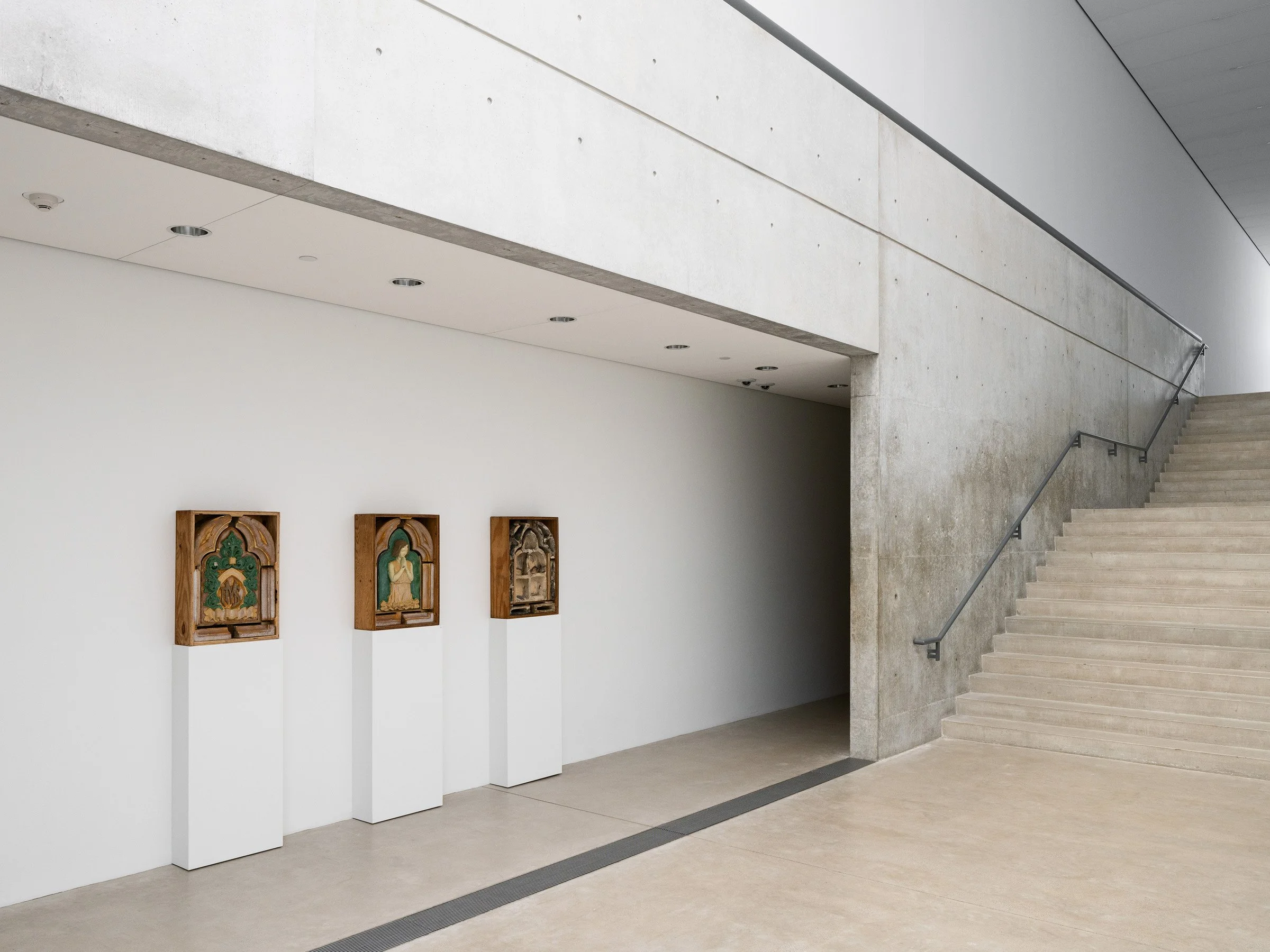 Pulitzer Arts Foundation interior showing three small carved reliefs on white pedestals beside the exposed concrete stair and smooth concrete walls, by Tadao Ando, St. Louis Missouri - architectural photographer St. Louis Missouri
