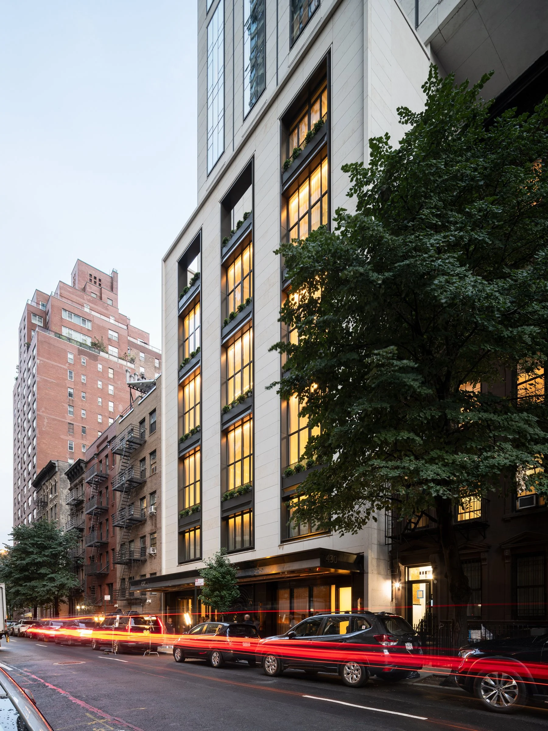 Sutton Tower street-level entry at dusk with warm light in the tall windows and traffic light trails along the side street, by Thomas Juul-Hansen, New York New York - architectural photographer
