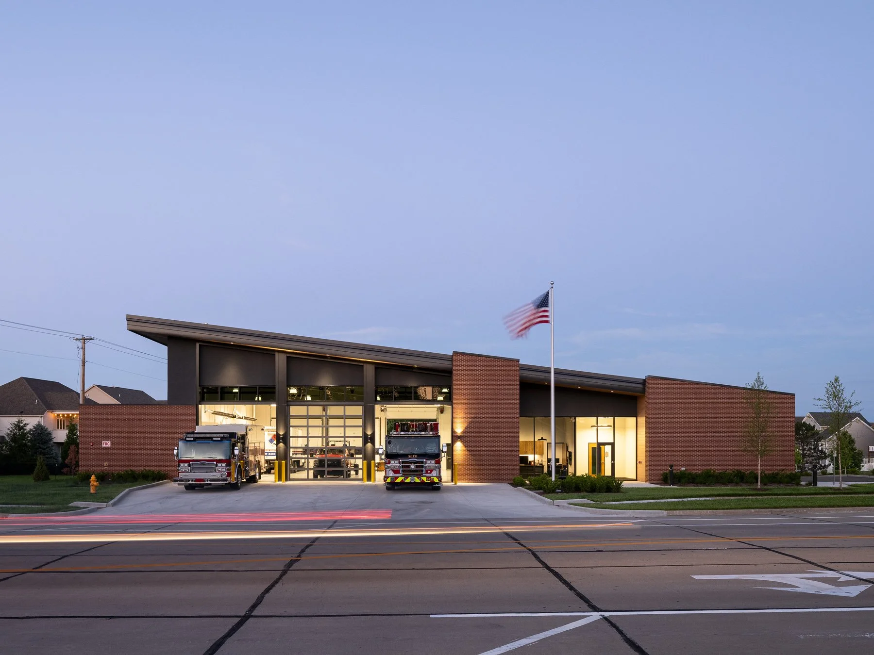 St. Charles fire station dusk front elevation with lit bays and flag, by JEMA, St. Charles Missouri - architectural photographer St. Louis Missouri