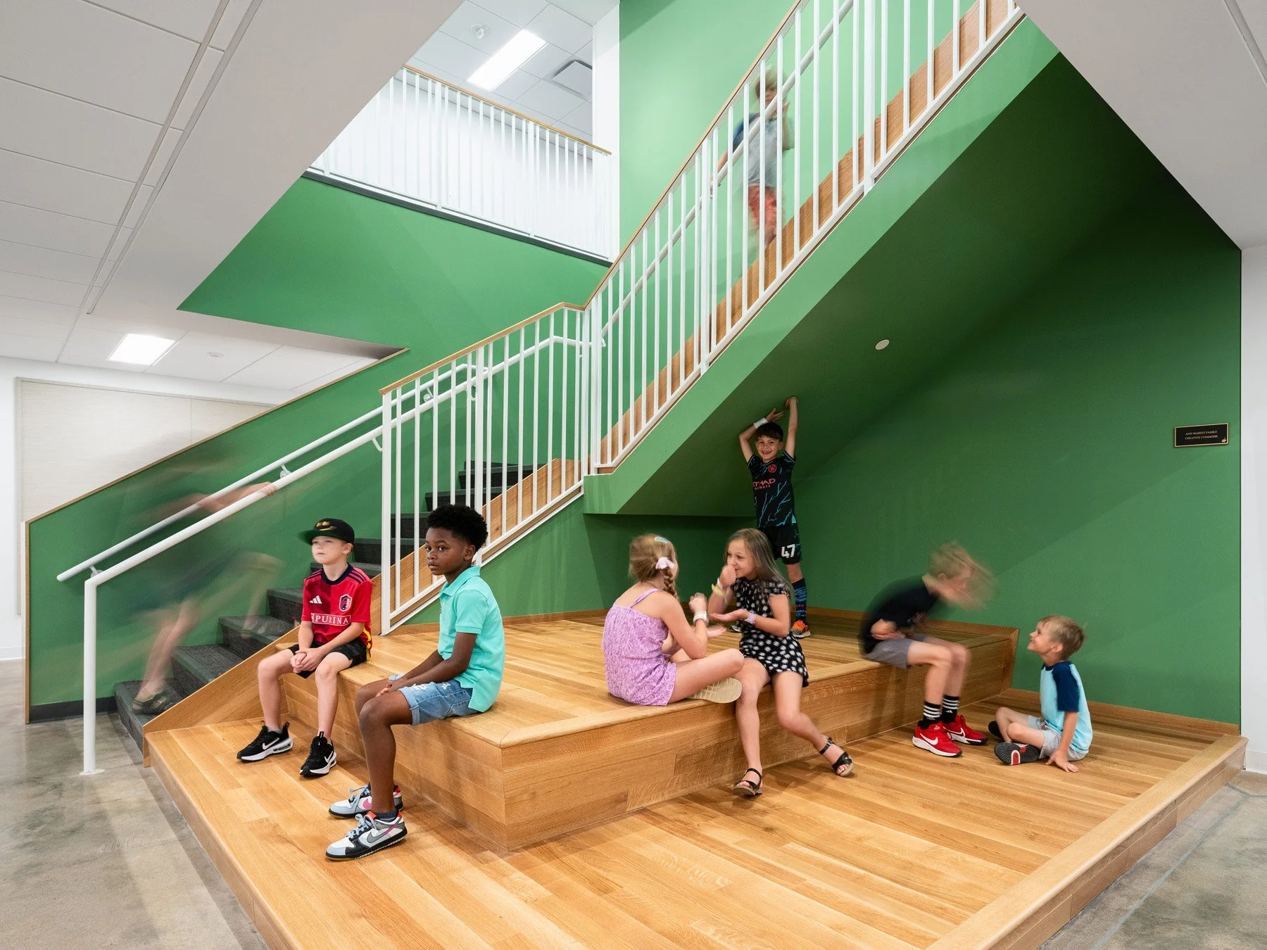 Broughton STEAM Center interior stair with tiered oak bleacher seating and green walls, by Christner - architectural photographer St. Louis Missouri