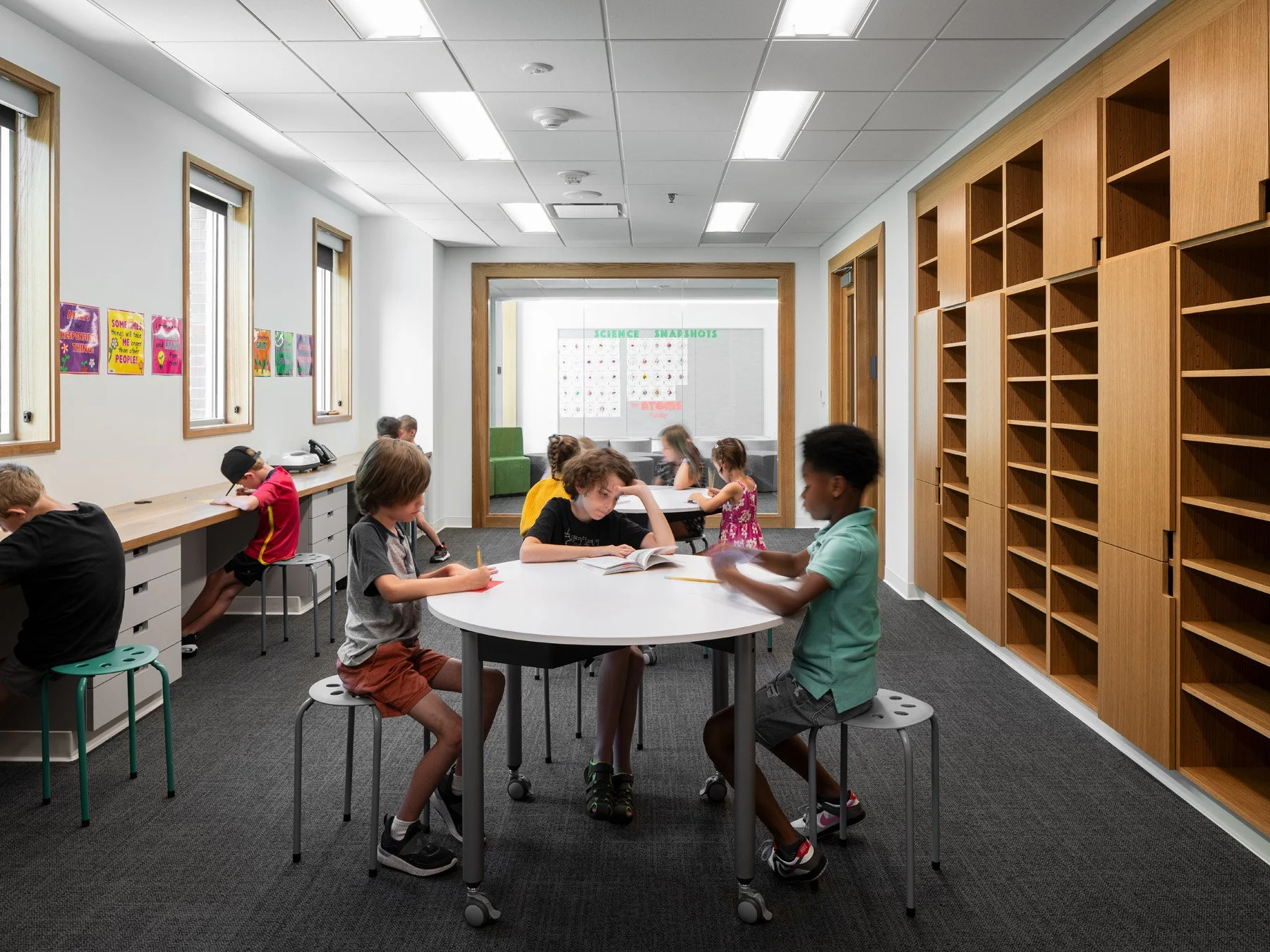 Broughton STEAM Center interior classroom with a round table and oak wall shelving, by Christner - architectural photographer St. Louis Missouri