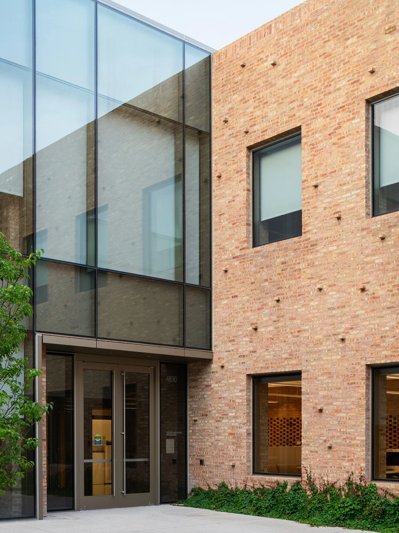 Chicago Park District HQ secondary entry at 4830 with glass volume above bronze doors and brick flanking wall - architectural photographer Chicago Illinois