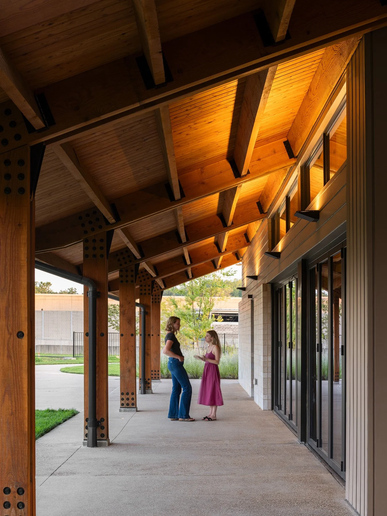 Brentwood Park Event Pavilion covered walkway at sunset with glowing timber ceiling and bolted columns, by Christner - architectural photographer St. Louis Missouri