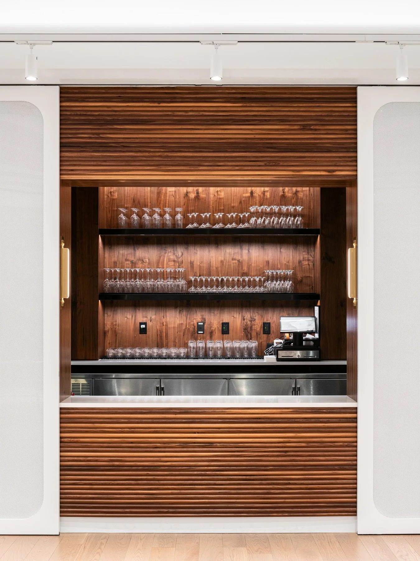 21c Museum Hotel interior gallery bar set in a recessed walnut niche stacked with glassware behind white perforated sliding panels, by Perfido Weiskopf Wagstaff + Goettel and Hufft - architectural photographer St. Louis Missouri