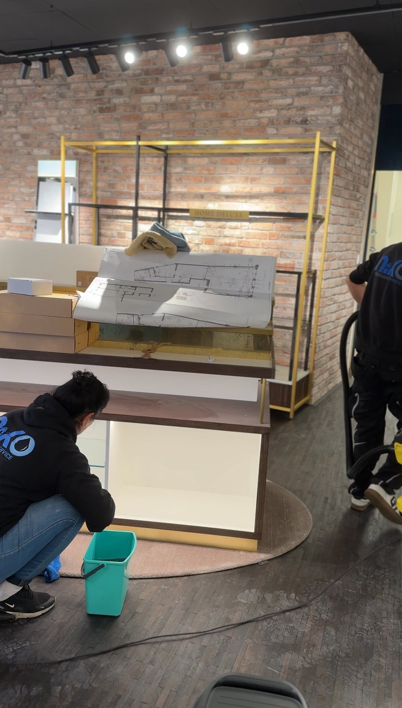 Mitarbeiter bei der Arbeit an einem Baumarktprojekt mit Bauplänen vor einer Backsteinwand, während sie Werkzeuge und Materialien vorbereiten.