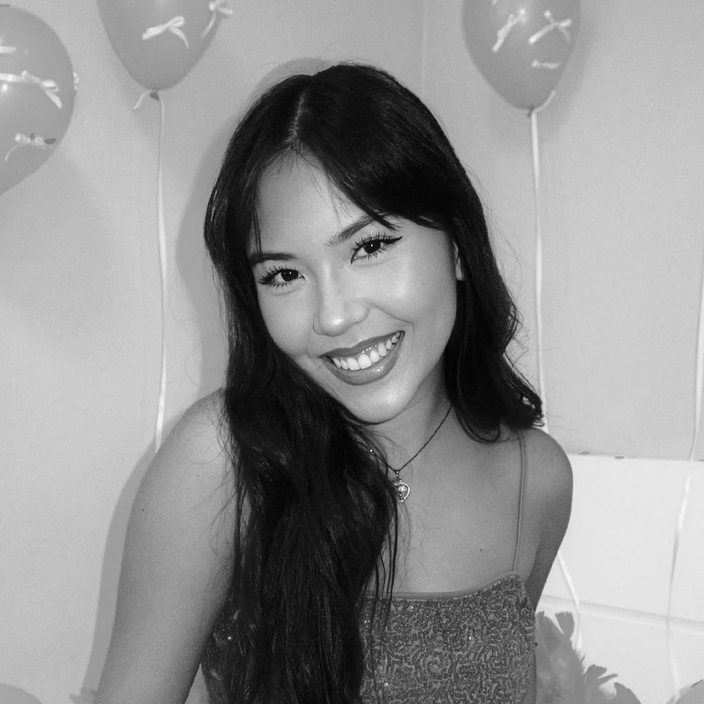 Retrato de uma mulher sorridente, com cabelo escuro e olhos fechados, usando uma camiseta com estampa brilhante na frente, em preto e branco.