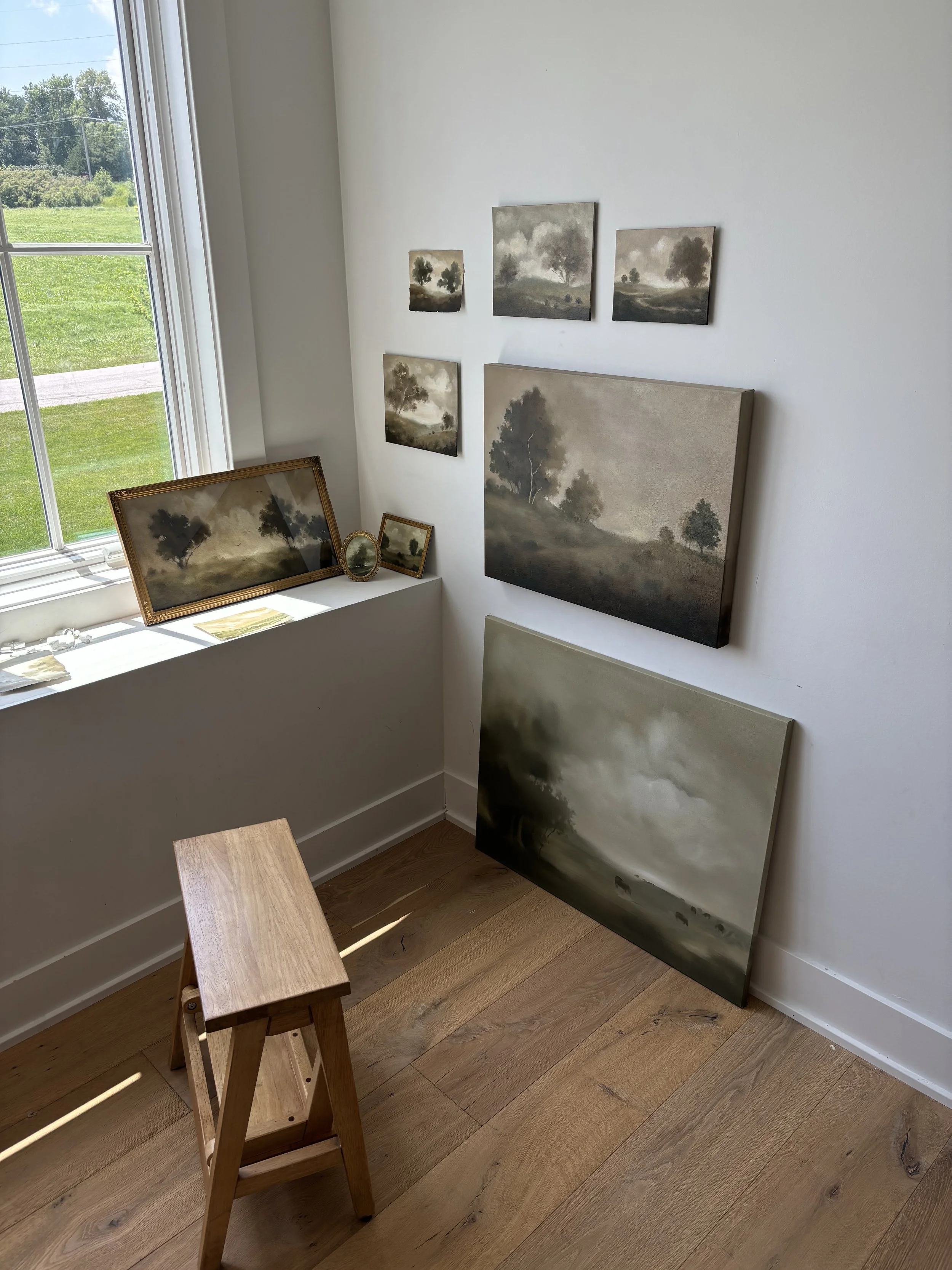 Interior of a room with landscape paintings on the walls and floor, a wooden stool, and a window showing an outdoor view.