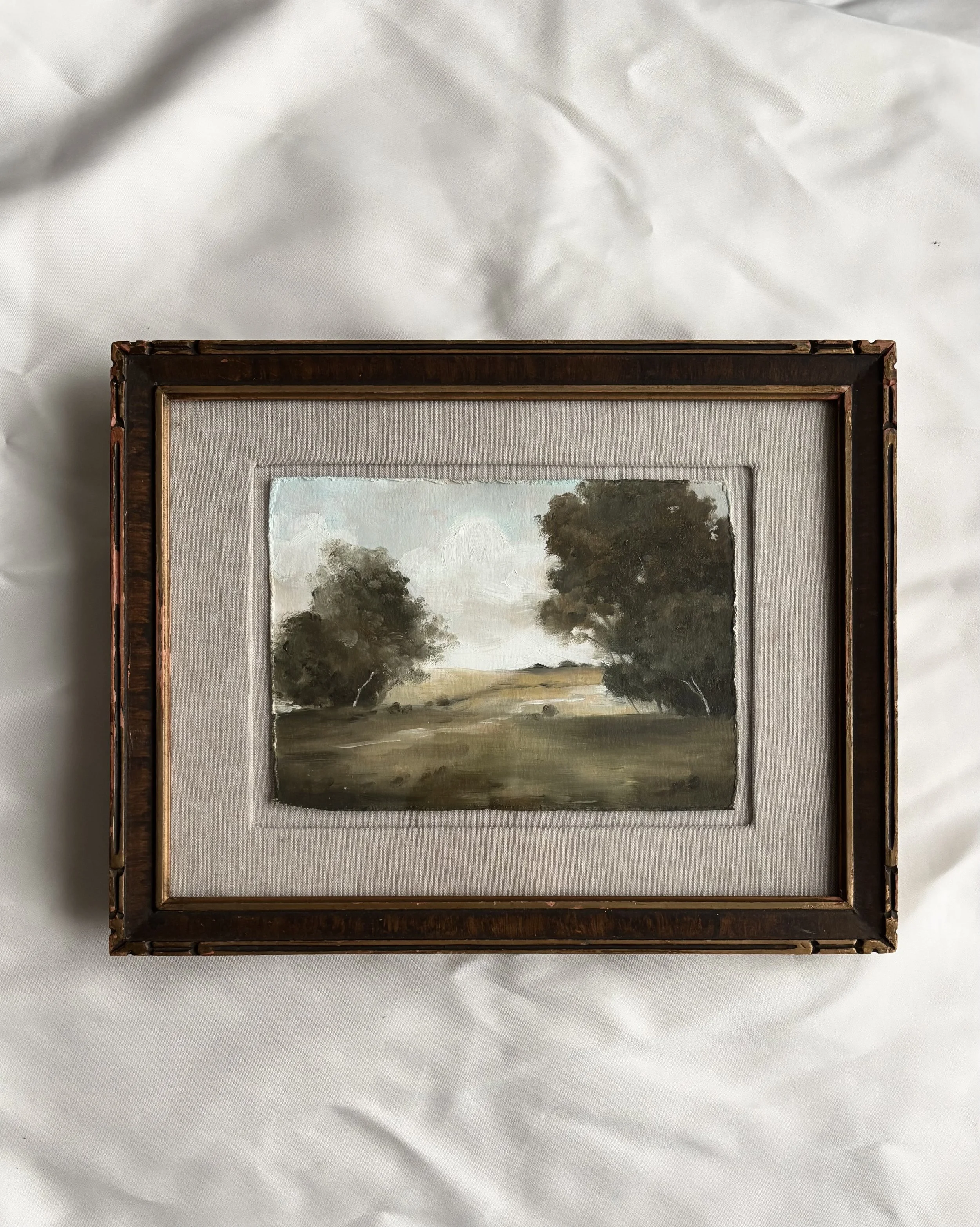Framed landscape painting with trees and open field.