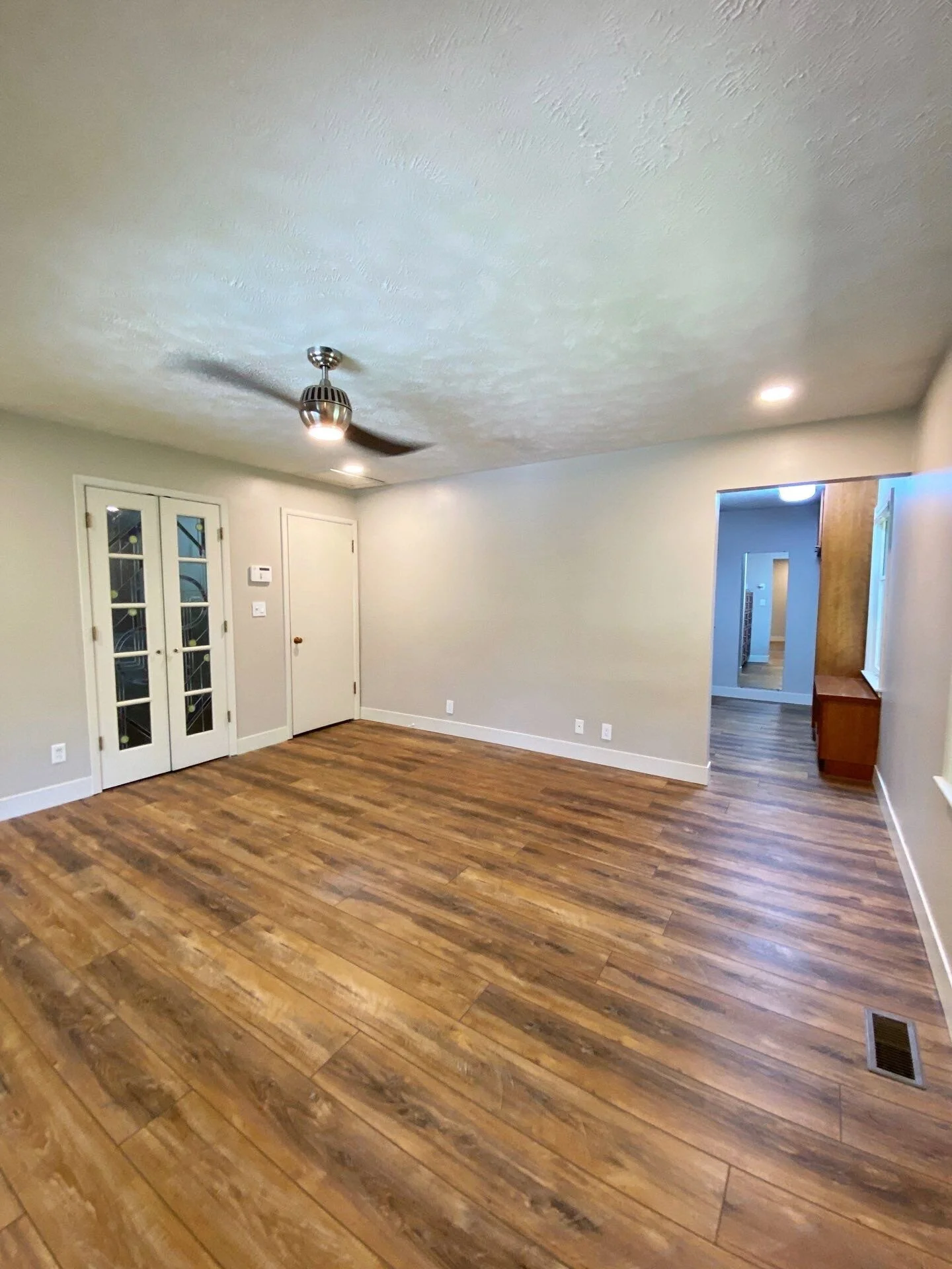 Empty living room with hardwood floors, beige walls, white trim, a ceiling fan, and double glass doors leading outside.