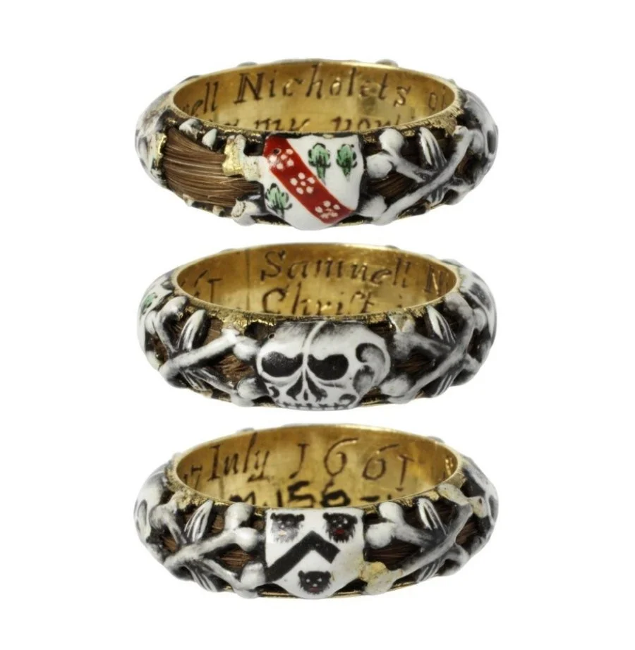 Antique memento mori mourning gold and enamel ring seen from 3 angles. The ring is hollow, and a lock of hair curls around within it, visible through the openwork of the enamelled skulls and coats of arms.