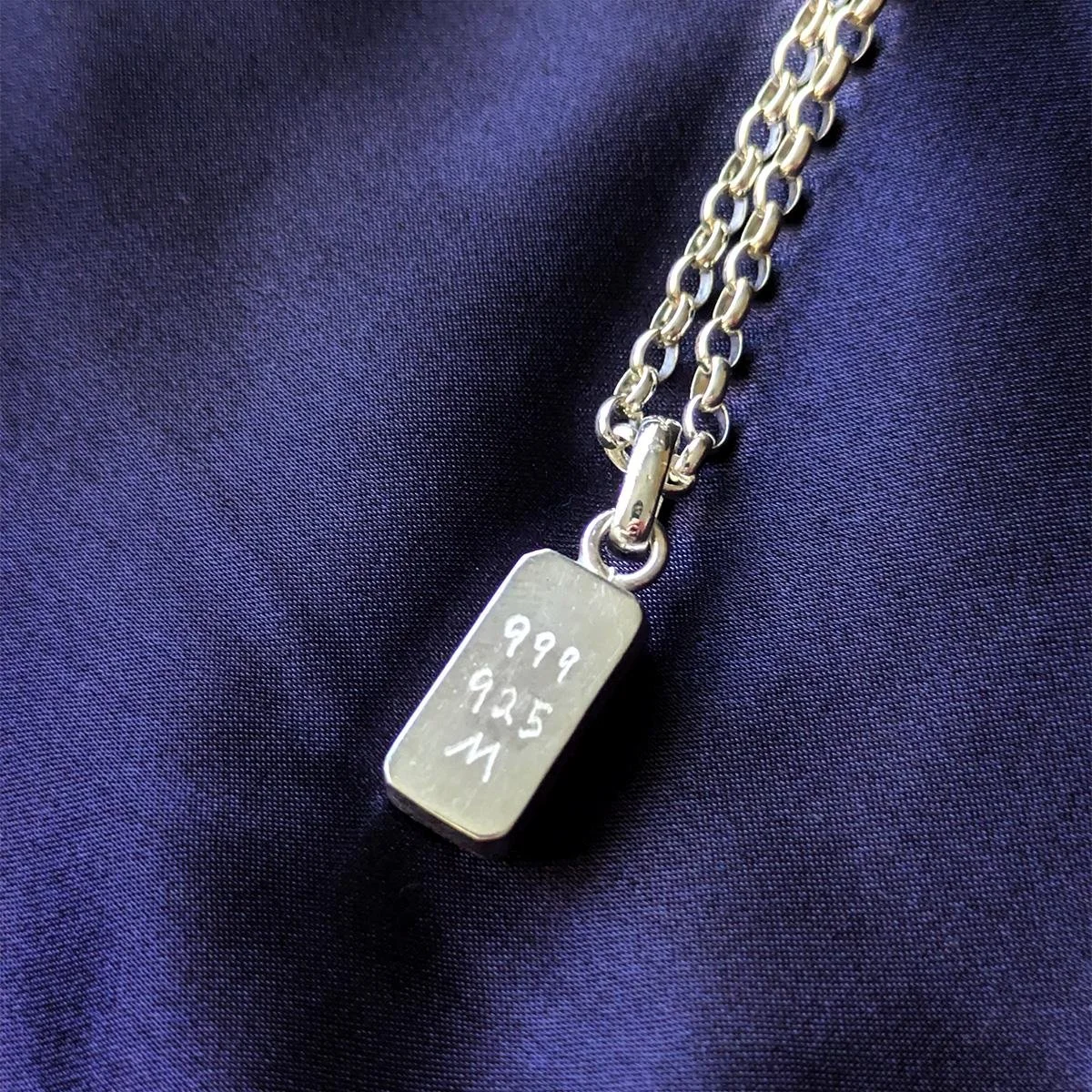 Close-up of the Ohad pendant back showing “999” and “925” marks and the Malki Studio “M,” on a sterling silver Belcher chain over dark navy fabric.