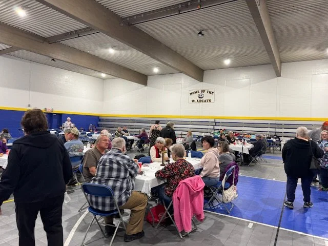 People sitting at tables in a gymnasium with a 