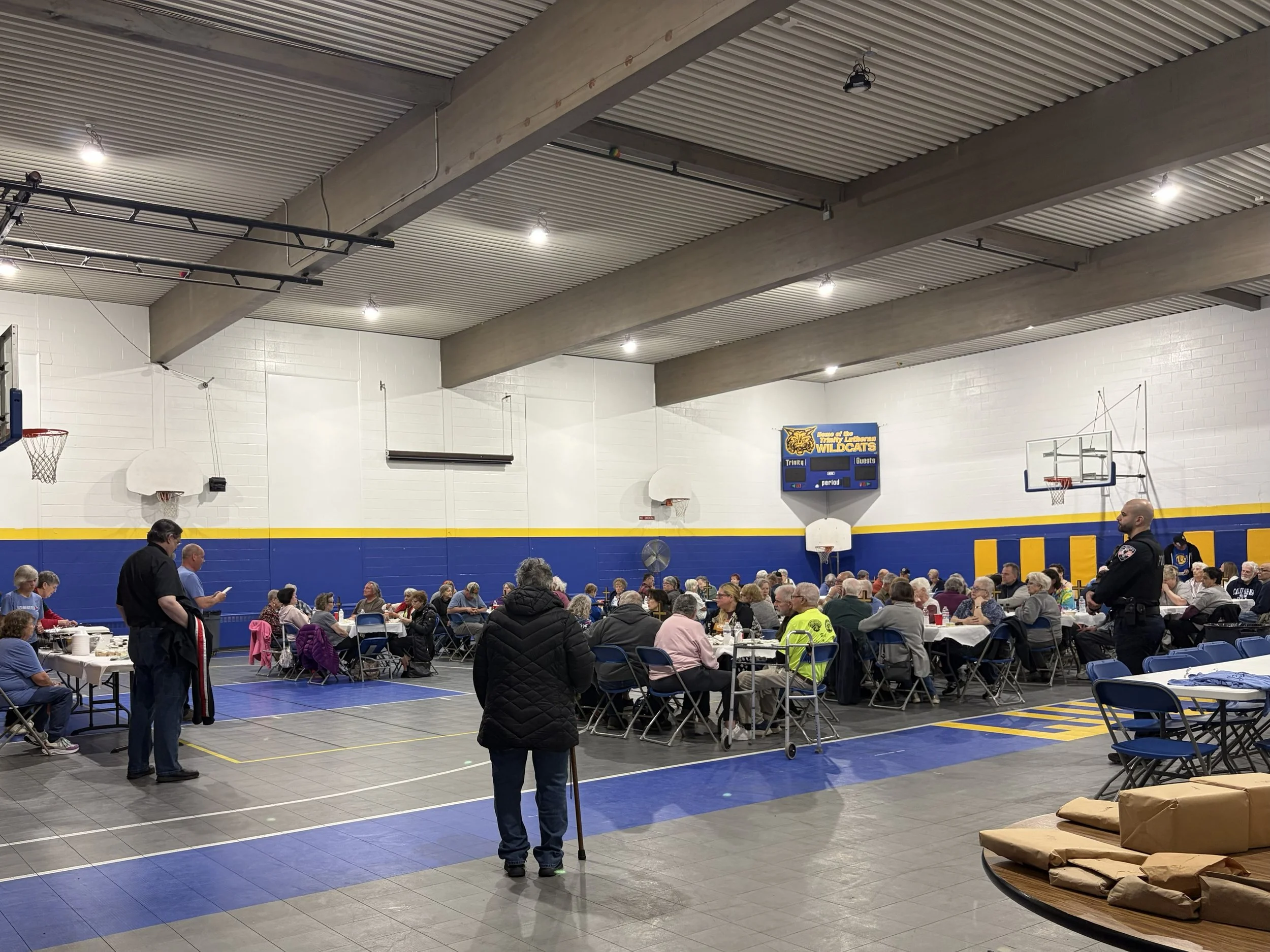 People gathered in a gymnasium with tables set up for a community meal.