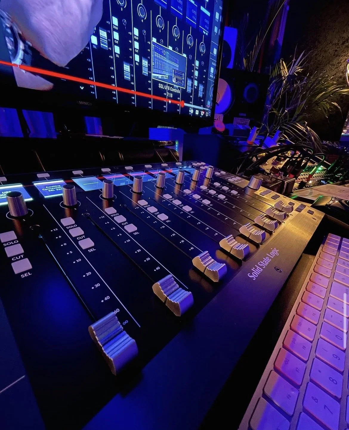 Solid State Logic control surface at the mixing desk under blue studio lighting.